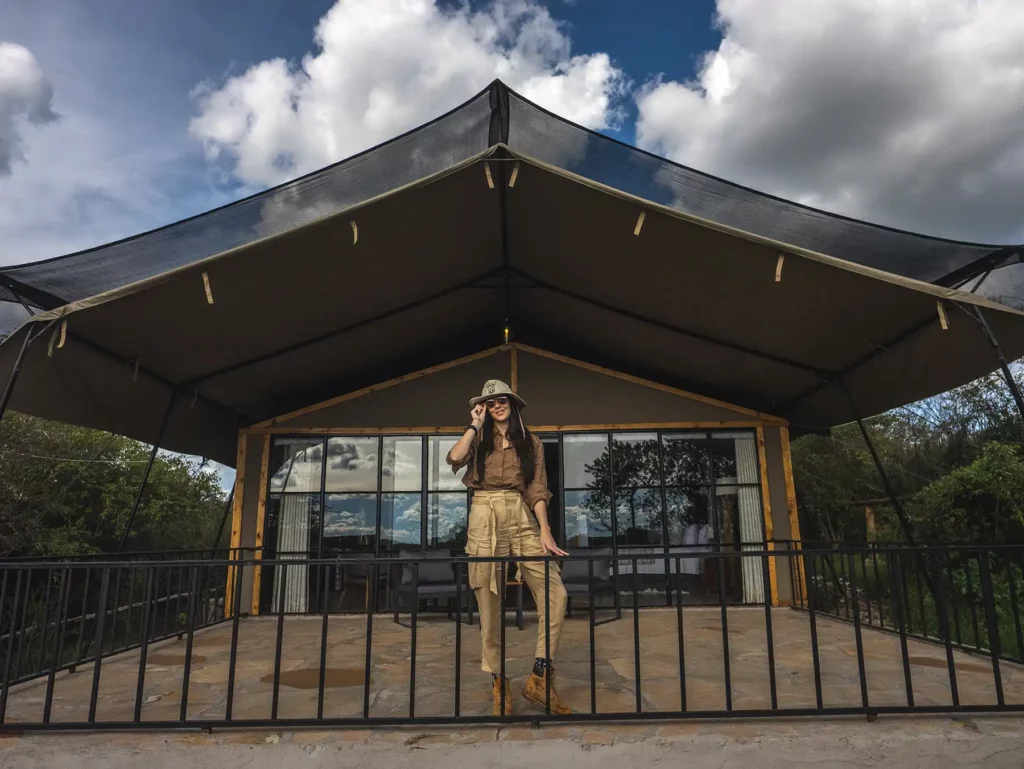 Ella Mckendrick standing in front of luxury safari tented accommodation with views across the Talek River to the Masai Mara, Kenya