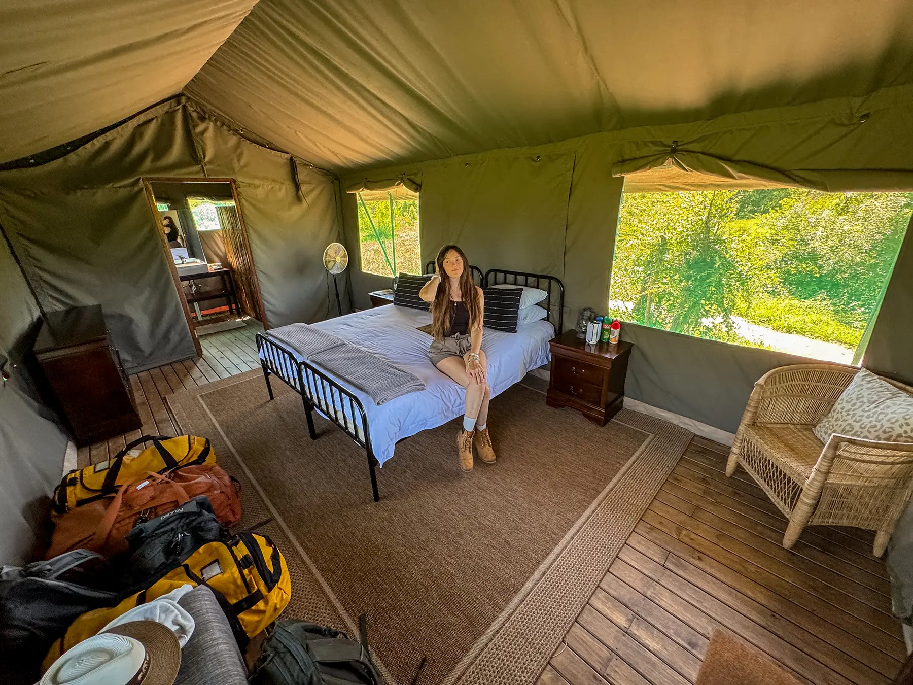 Ella McKendrick sitting on a double bed inside a canvas safari tent with green vegetation visible through the open windows on safari in the Manyeleti Game Reserve, South Africa