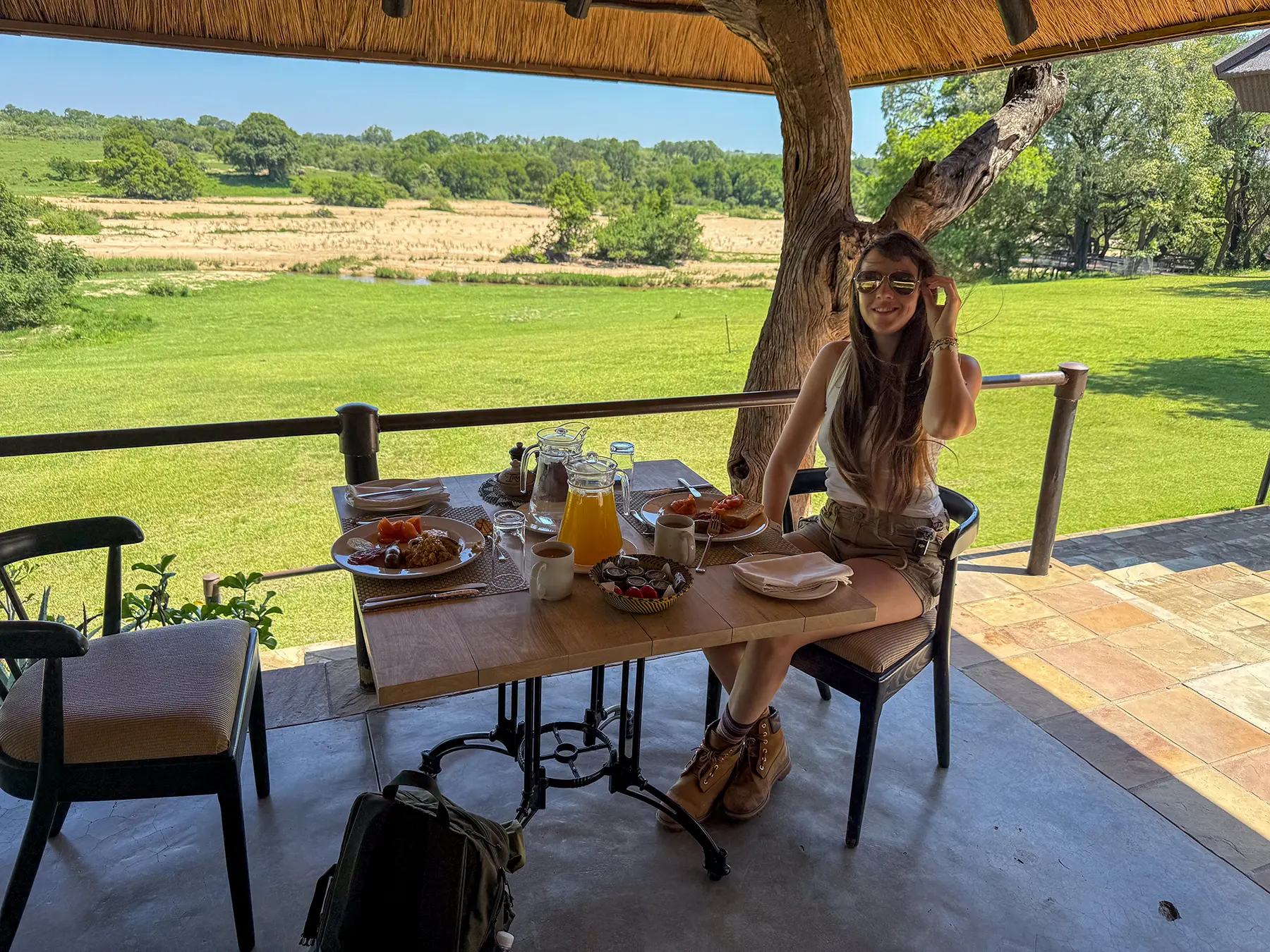 Ella McKendrick having breakfast on the riverside terrace with green lawns and the river beyond on safari in Sabi Sand Game Reserve, South Africa