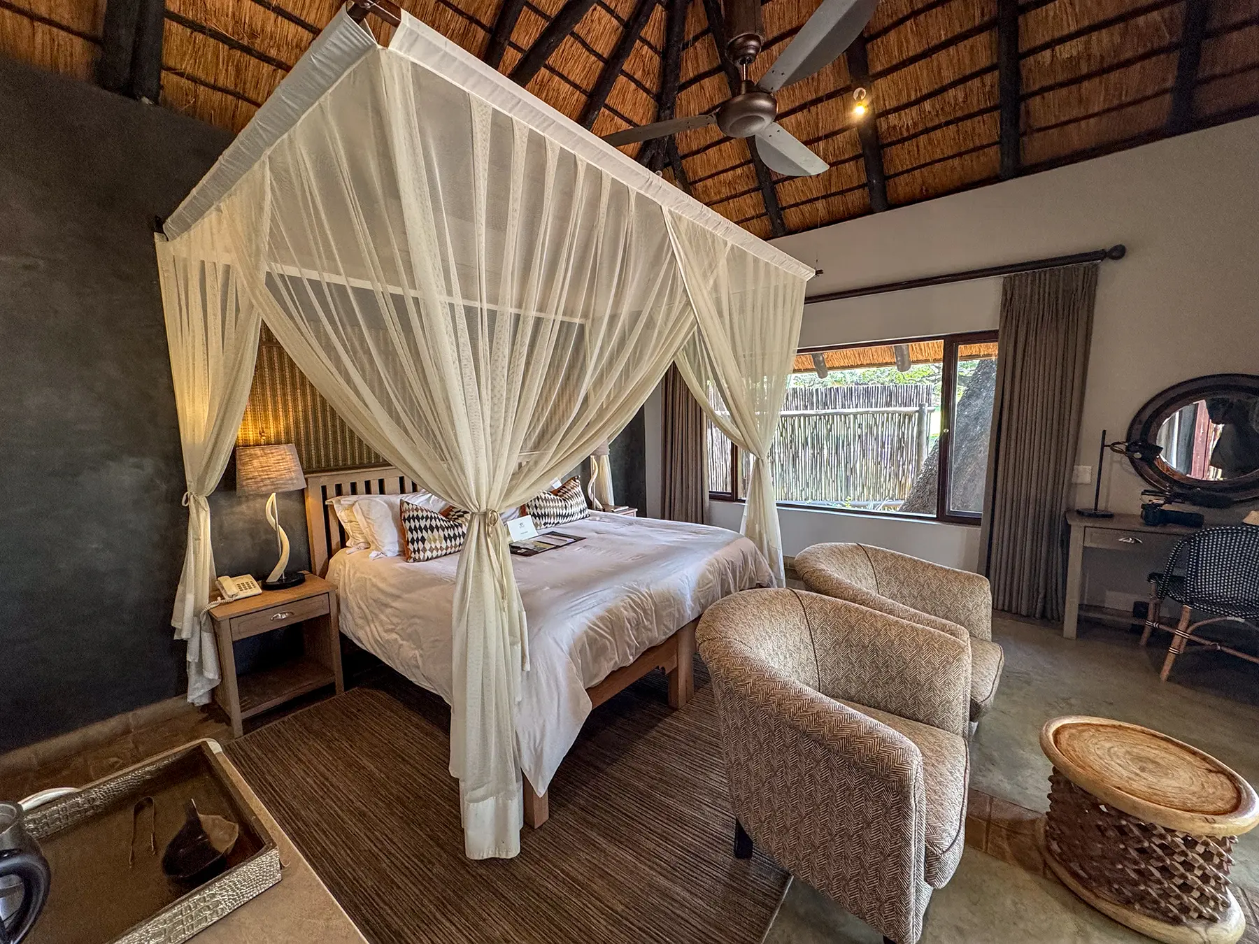 Safari suite with a draped canopy bed, thatched ceiling, and upholstered armchairs on safari in Sabi Sand Game Reserve, South Africa