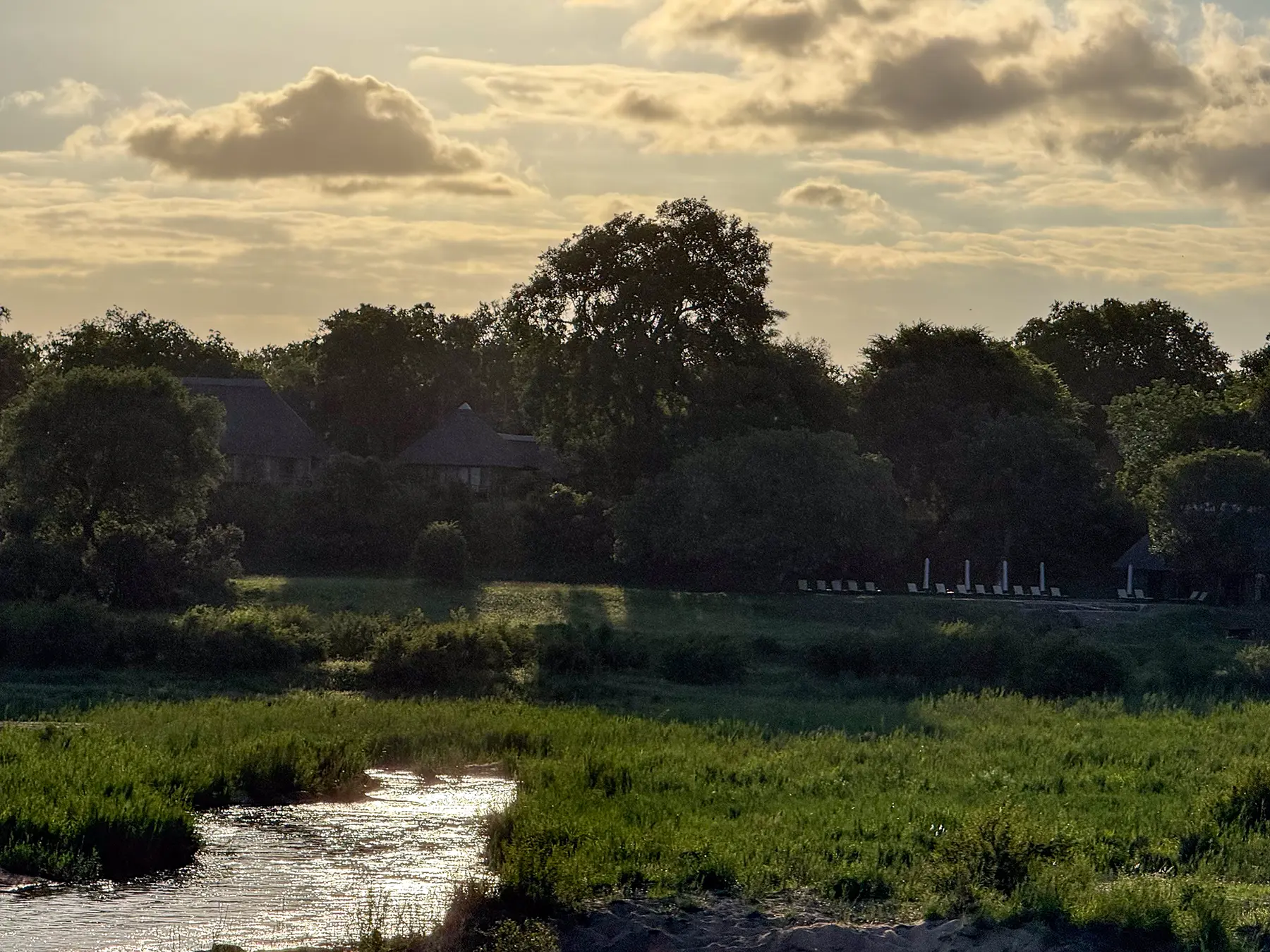 A panoramic view of a safari lodge on the banks of a river at sunset, with lush green vegetation and golden light reflecting off the water on safari in Sabi Sand Game Reserve, South Africa