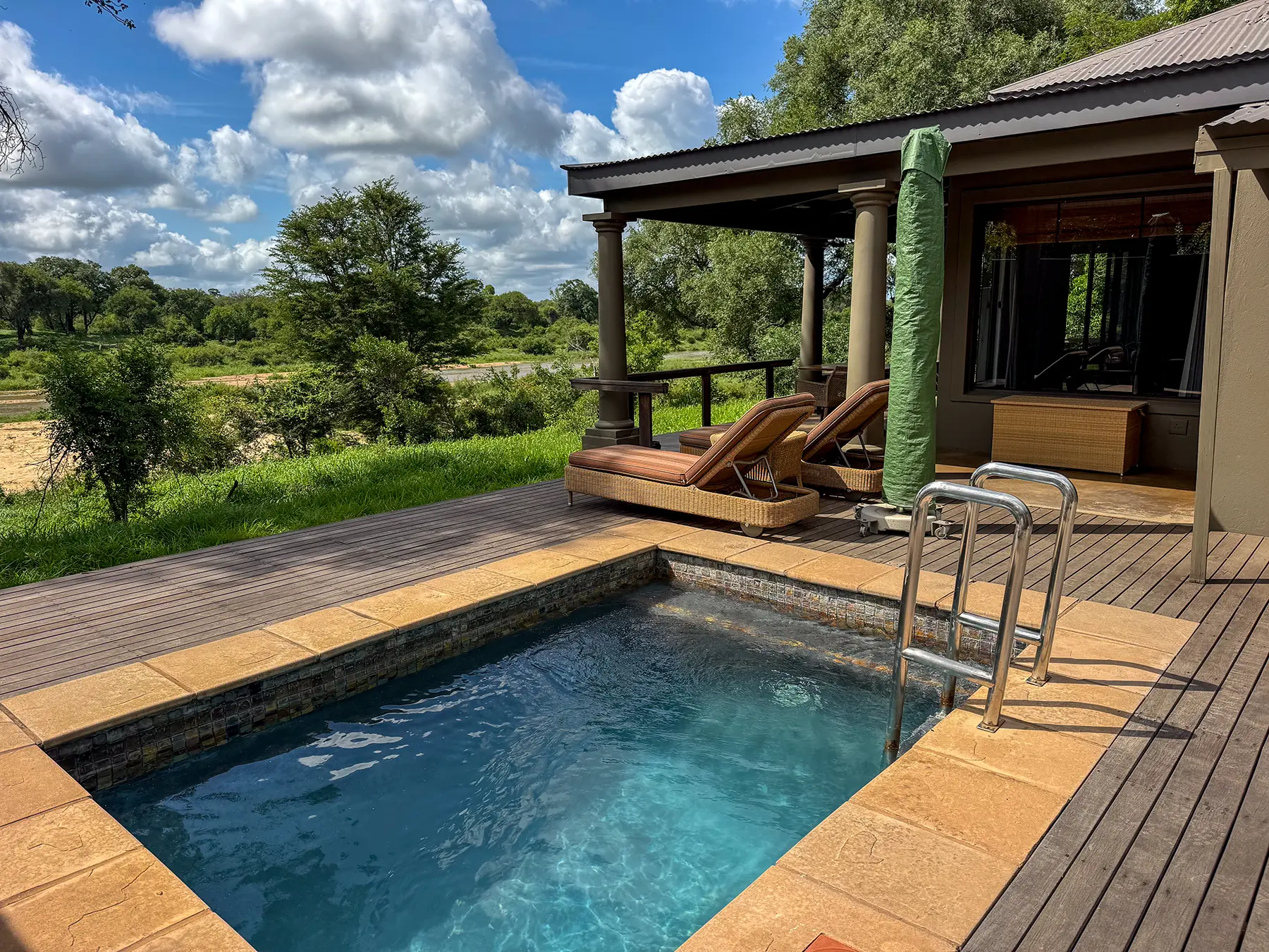 Private plunge pool on a wooden deck with sun loungers overlooking green bush and a river at a luxury safari lodge in Sabi Sand Game Reserve, South Africa