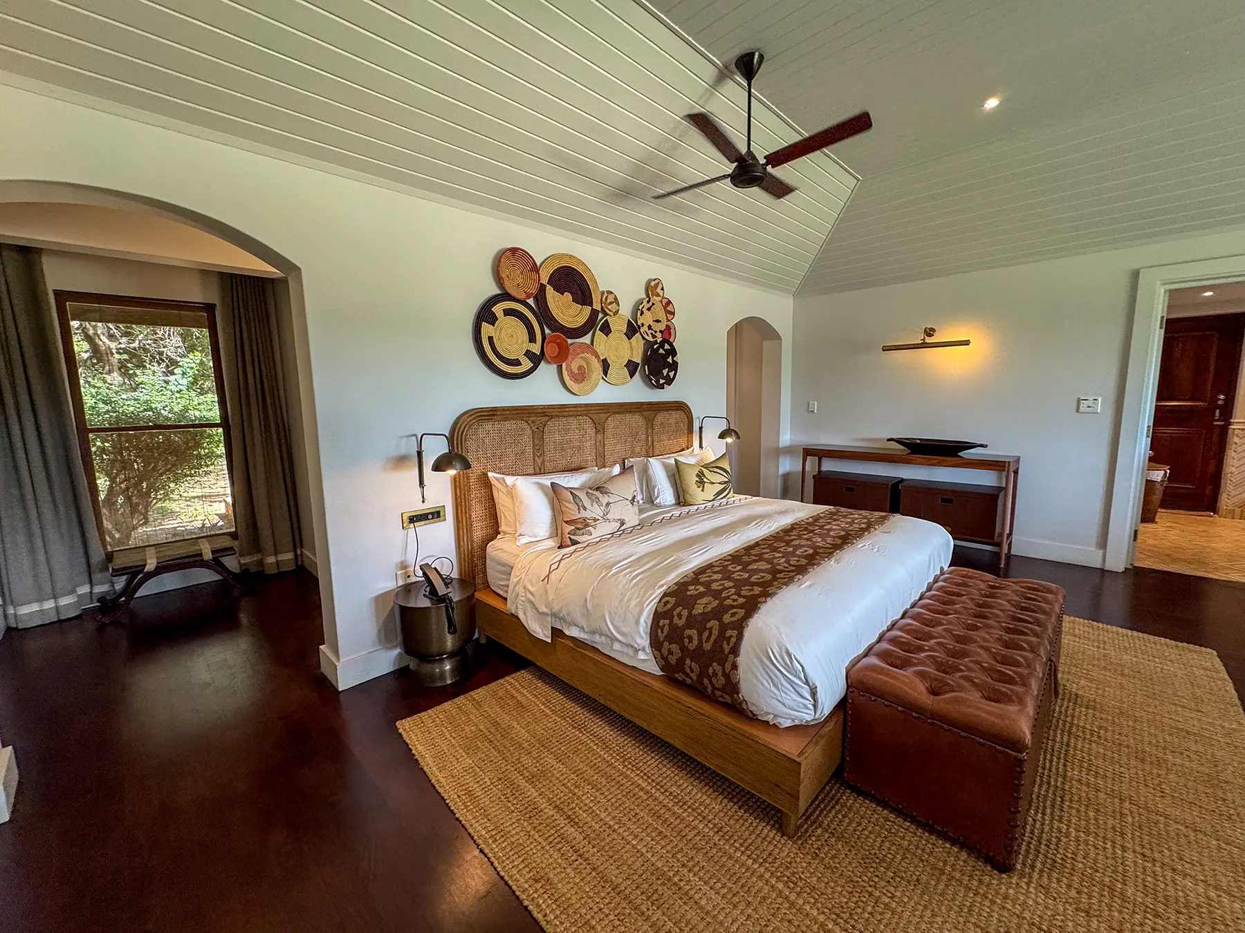 Spacious bedroom with a king-size bed, woven rattan headboard and decorative wall plates at a luxury safari lodge in Sabi Sand Game Reserve, South Africa