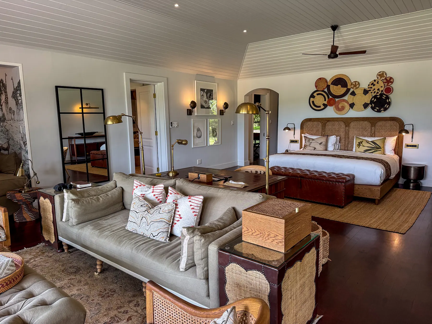 Open-plan suite with a sofa, woven armchairs and a king-size bed with decorative wall art at a luxury safari lodge in Sabi Sand Game Reserve, South Africa