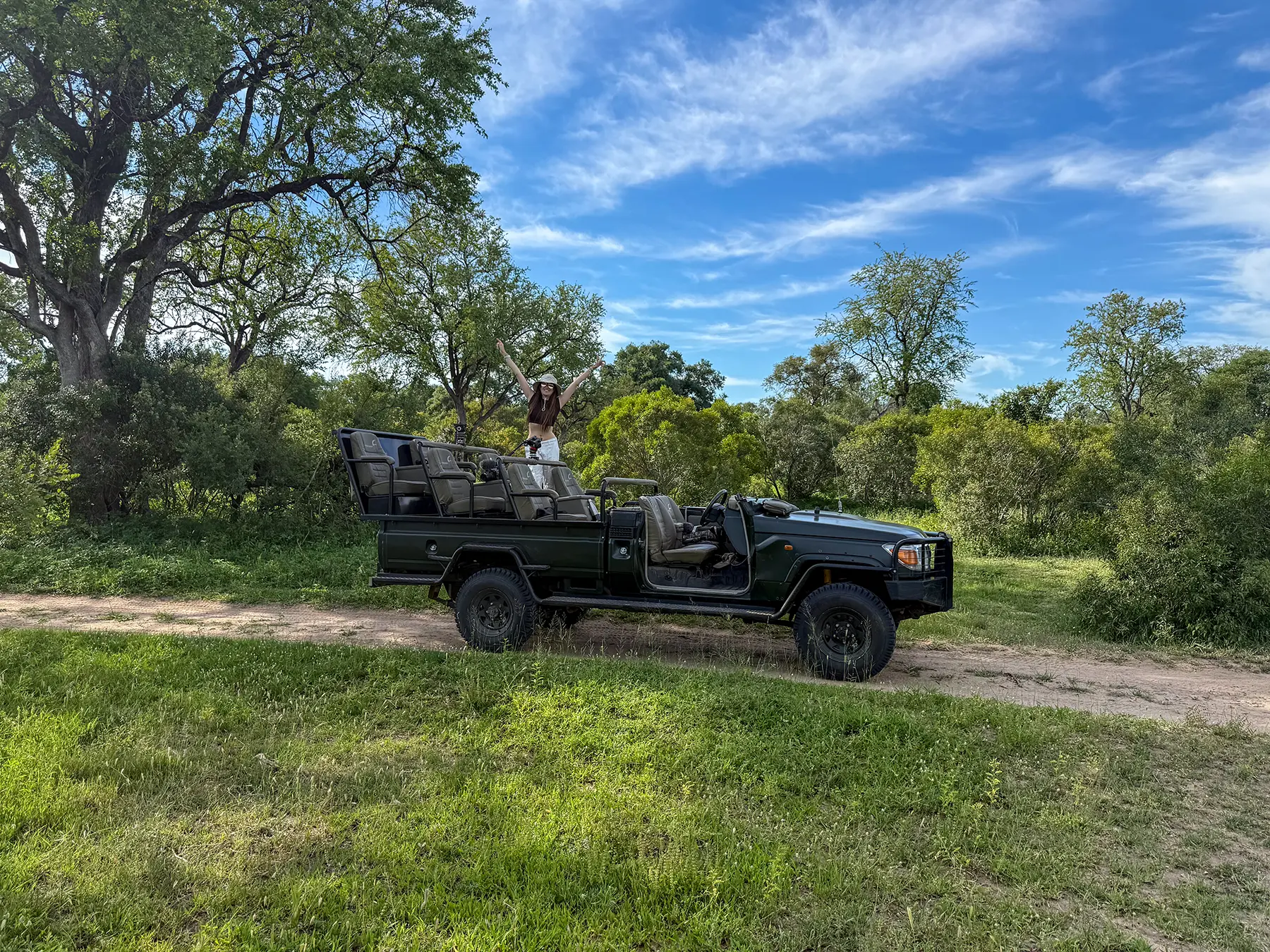 Ella McKendrick standing on a green Land Cruiser safari vehicle in lush woodland on safari in Sabi Sand Game Reserve, South Africa