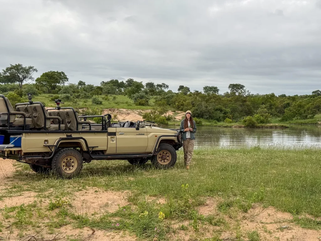 Ella McKendrick standing beside a game drive vehicle at the riverside on safari in the Sabi Sand Game Reserve, South Africa