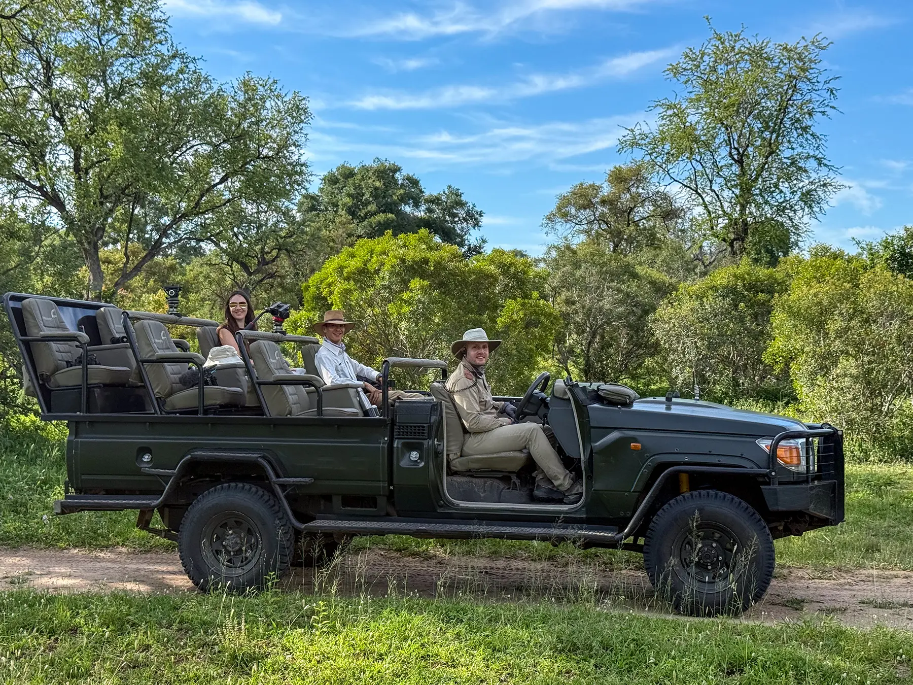 Ella McKendrick seated in an open safari Land Cruiser with a guide driving and a tracker in the front seat surrounded by green bushveld on safari in Sabi Sand Game Reserve, South Africa