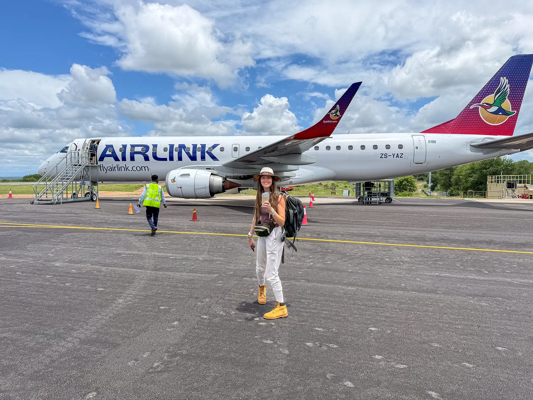 Ella McKendrick standing on the tarmac in front of an Airlink Embraer jet with passengers boarding behind her at Skukuza Airport in Kruger National Park, South Africa