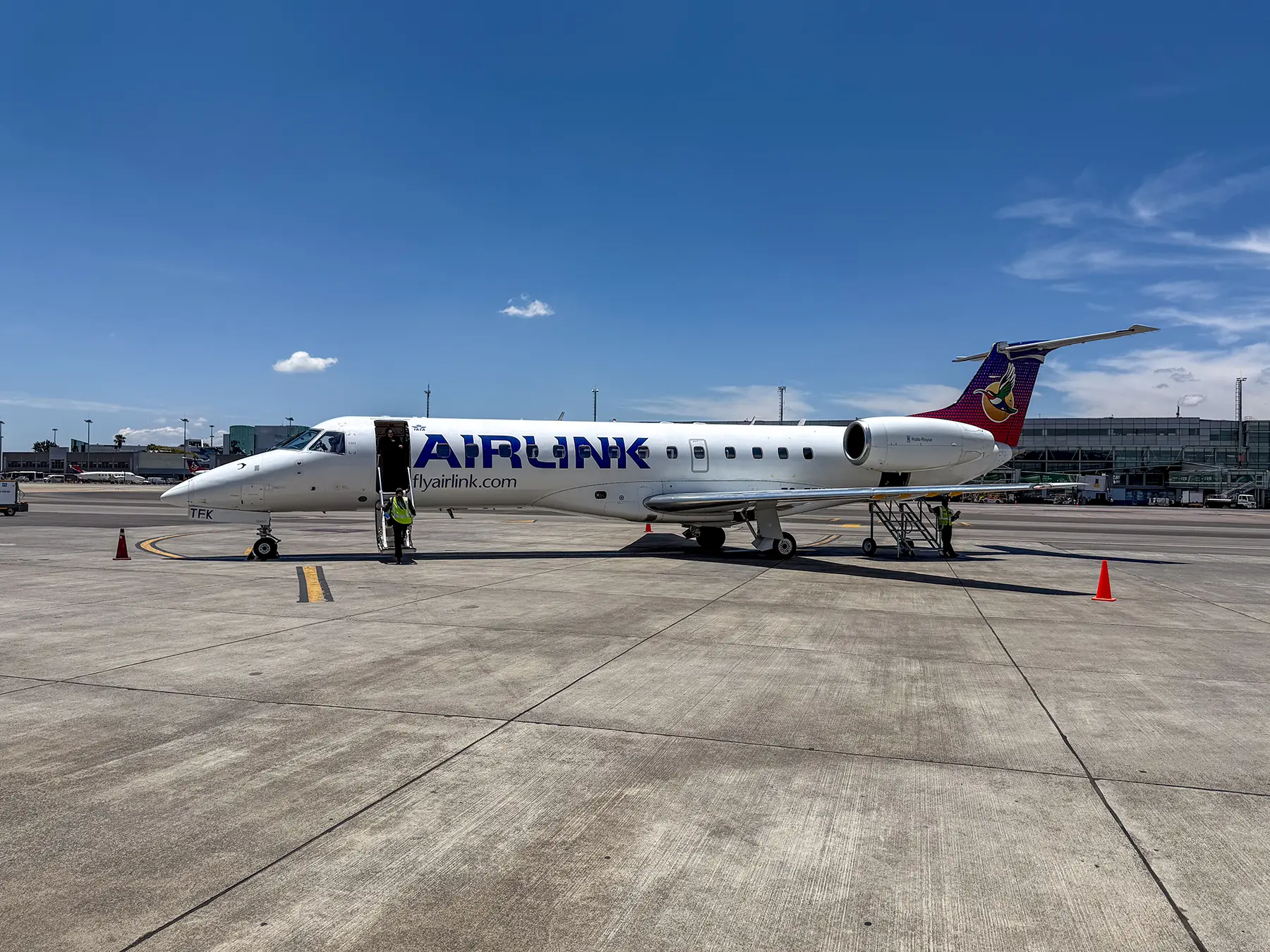 An Airlink Embraer regional jet parked on the tarmac with ground crew nearby on a flight in South Africa