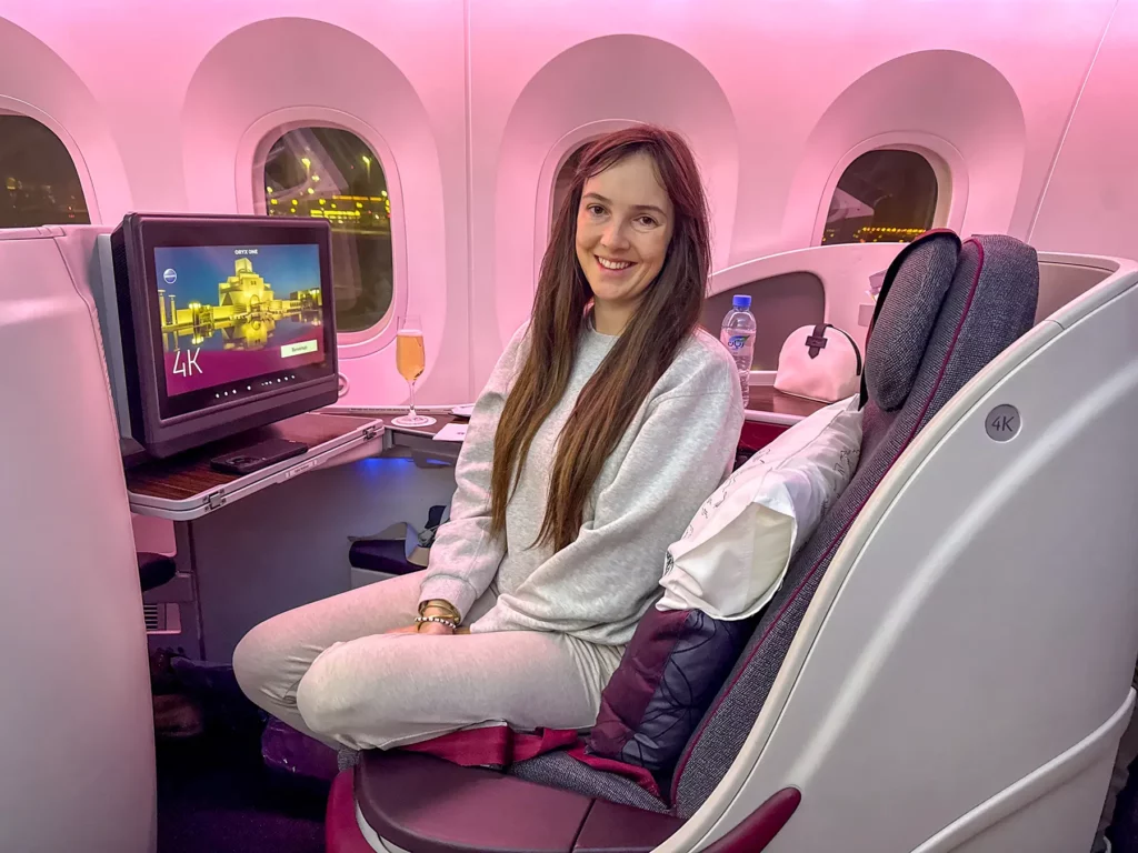 Ella McKendrick sitting comfortably in a business class seat with pink mood lighting and an entertainment screen on a flight to South Africa