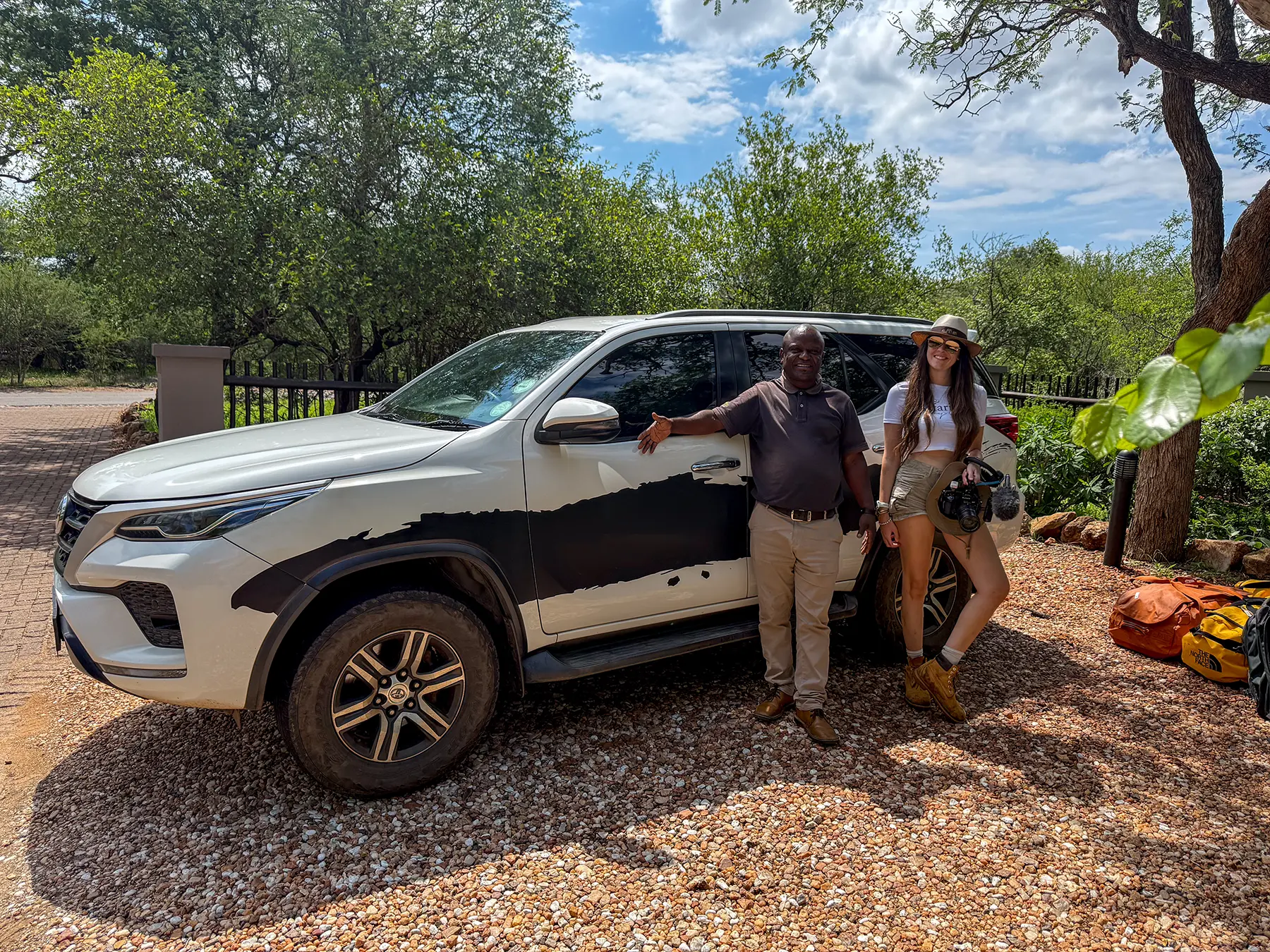 Ella McKendrick and her transfer driver standing together beside a white Toyota Fortuner at a safari lodge in South Africa