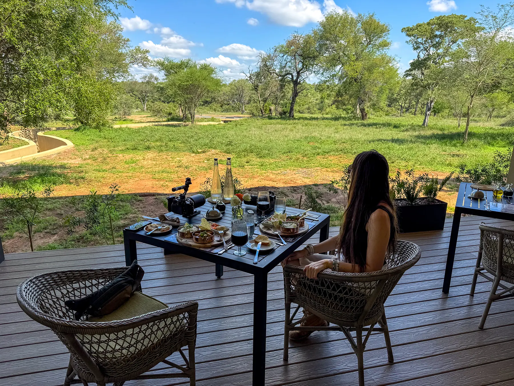 Ella McKendrick dining on a lodge deck with a full lunch spread, wine and views across green bushveld on safari in the Timbavati Private Nature Reserve, South Africa