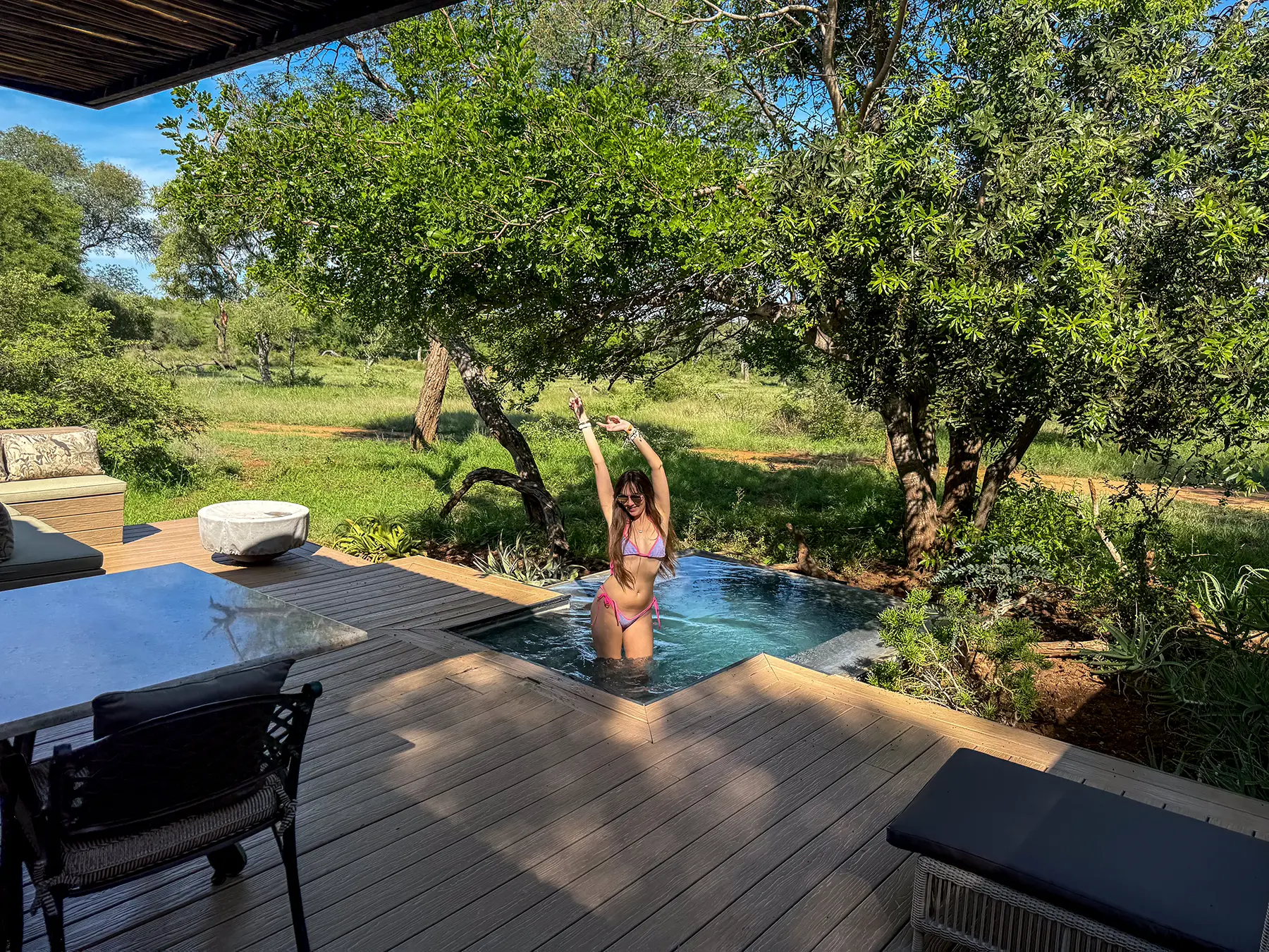 Ella McKendrick standing in a private plunge pool on a wooden deck surrounded by green bushveld on safari in the Timbavati Private Nature Reserve, South Africa