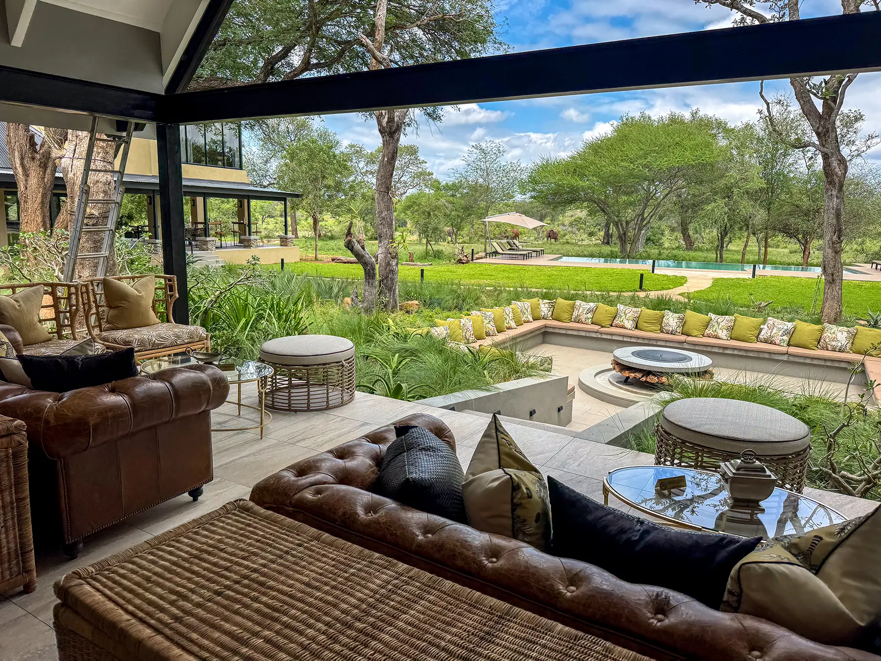 A covered lounge area with leather Chesterfield sofas and cushioned seating overlooking a swimming pool and green bushveld on safari in the Timbavati Private Nature Reserve, South Africa