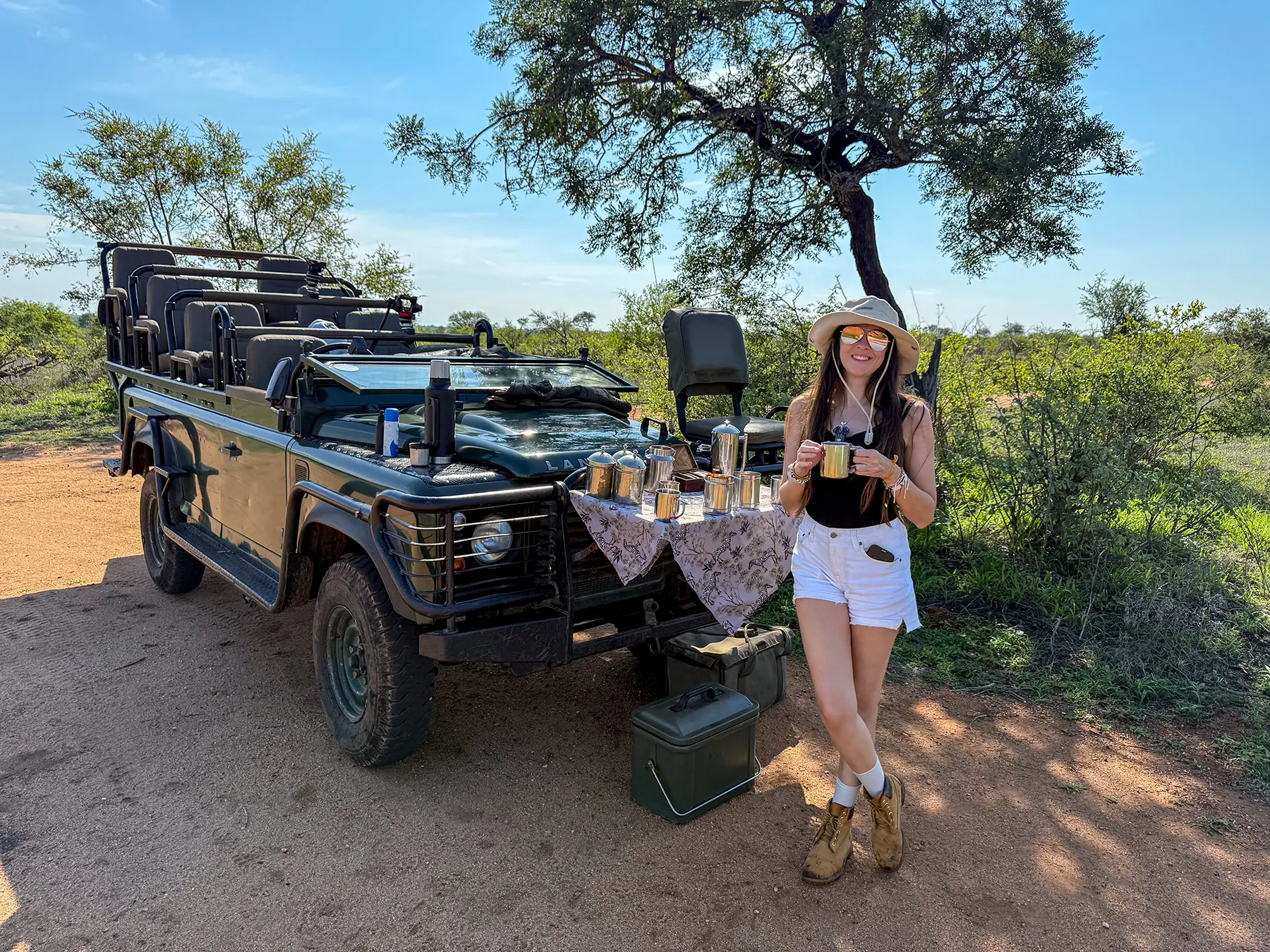Ella McKendrick holding a coffee mug beside a safari vehicle during a bush coffee stop on safari in the Timbavati Private Nature Reserve, South Africa