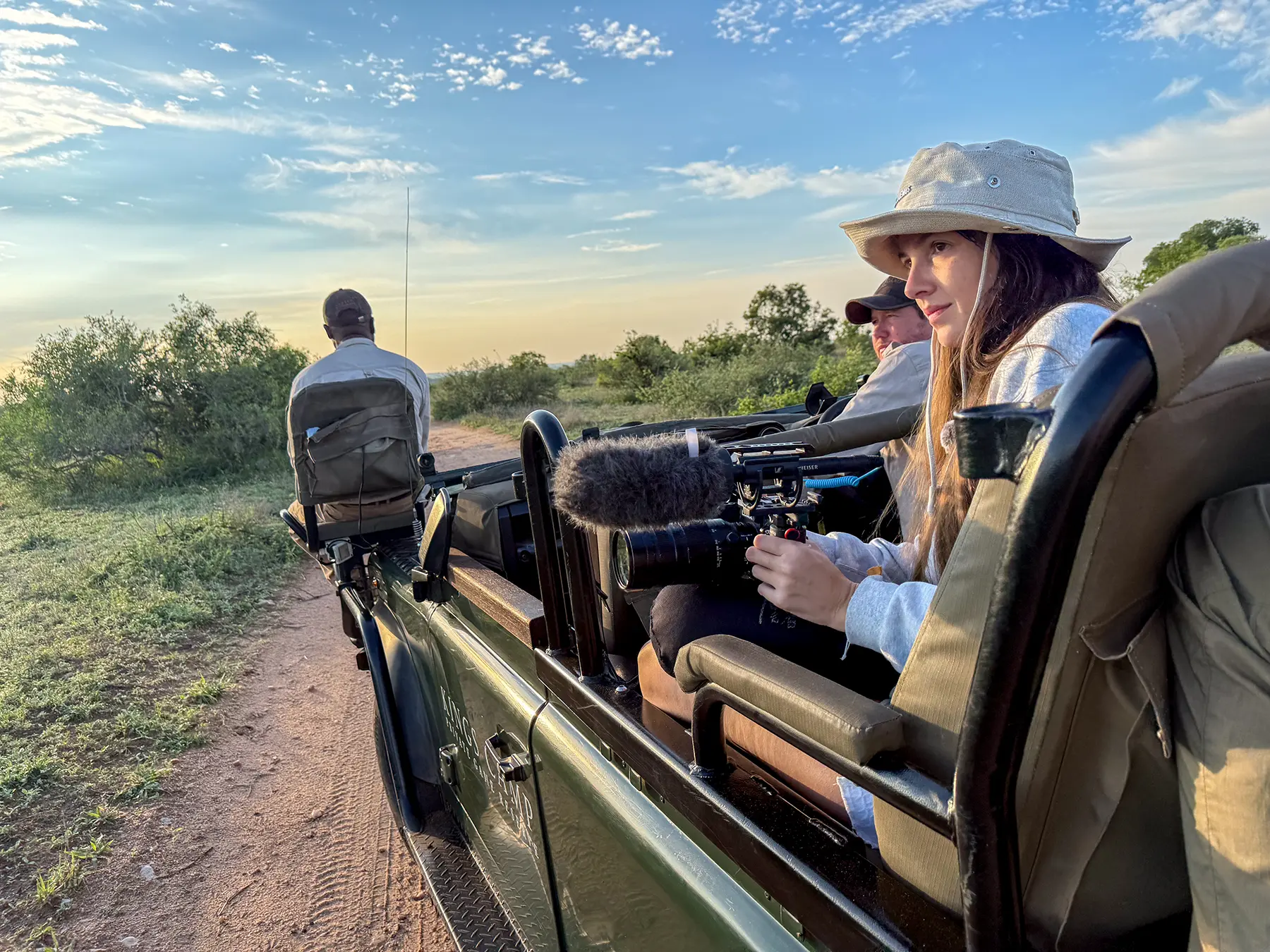 Ella McKendrick filming with a camera and microphone from a safari vehicle at sunset on safari in the Timbavati Private Nature Reserve, South Africa