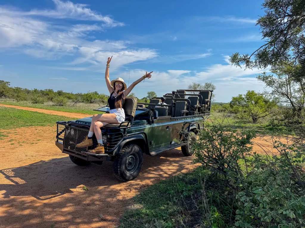 Ella McKendrick posing with arms raised on the bonnet of a safari vehicle on safari in the Timbavati Private Nature Reserve, South Africa