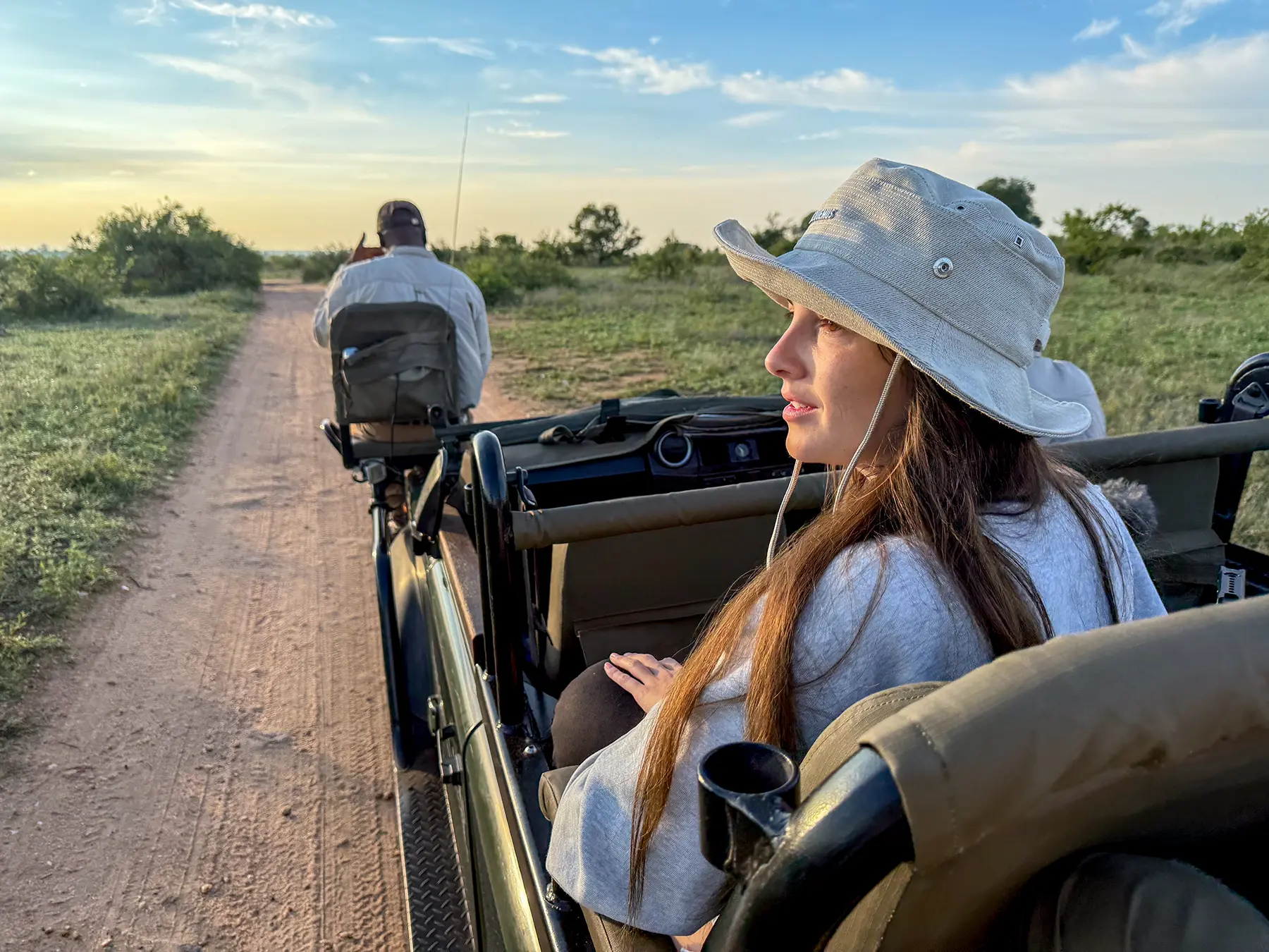 Ella McKendrick sitting in the back of a safari vehicle at sunset with the tracker ahead on safari in the Timbavati Private Nature Reserve, South Africa