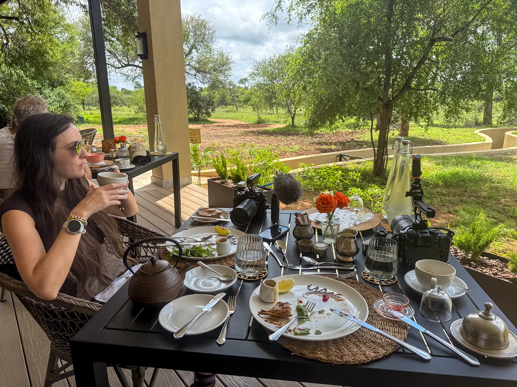 Ella McKendrick having breakfast on a lodge terrace with camera equipment and a bush view at a safari lodge in the Timbavati Private Nature Reserve, South Africa