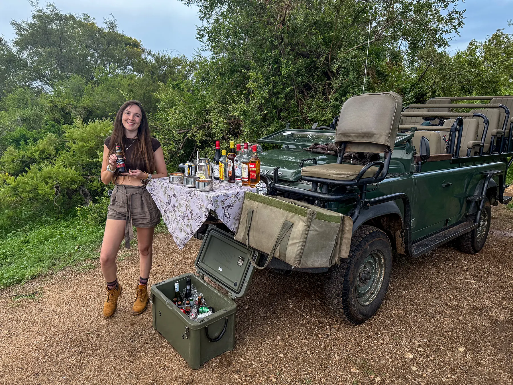 Ella McKendrick standing beside a sundowner drinks setup on the tailgate of a safari vehicle on safari in the Timbavati Private Nature Reserve, South Africa
