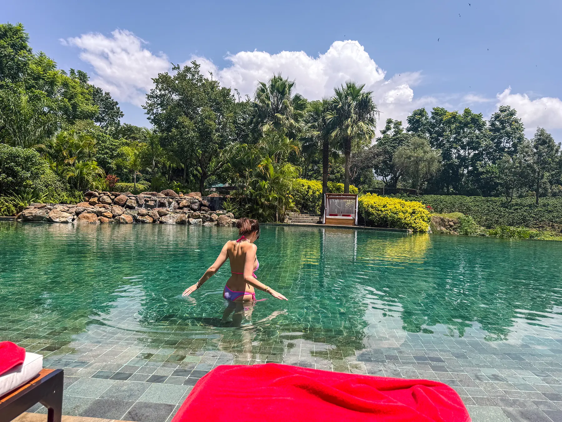 Ella McKendrick wading in a hotel pool surrounded by tropical gardens in Arusha, Tanzania