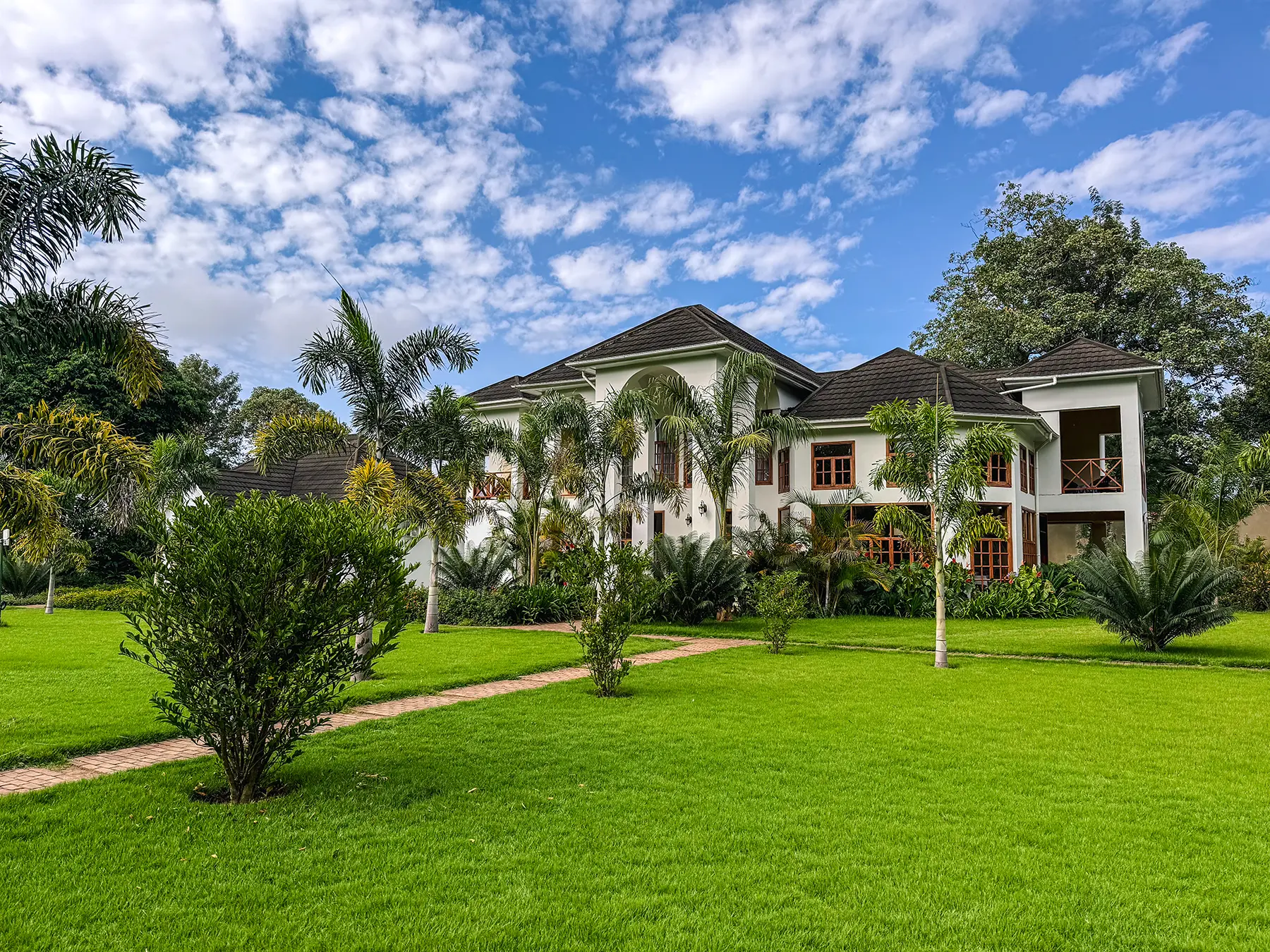 A white two-storey lodge building with palm trees and manicured lawns under a blue sky in Arusha, Tanzania