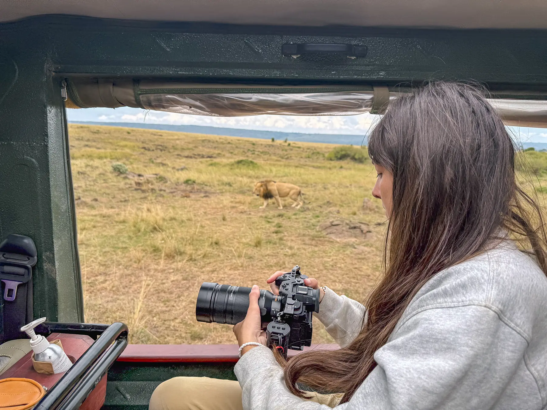 Ella McKendrick photographing a lion from a safari vehicle in Maasai Mara National Reserve, Kenya
