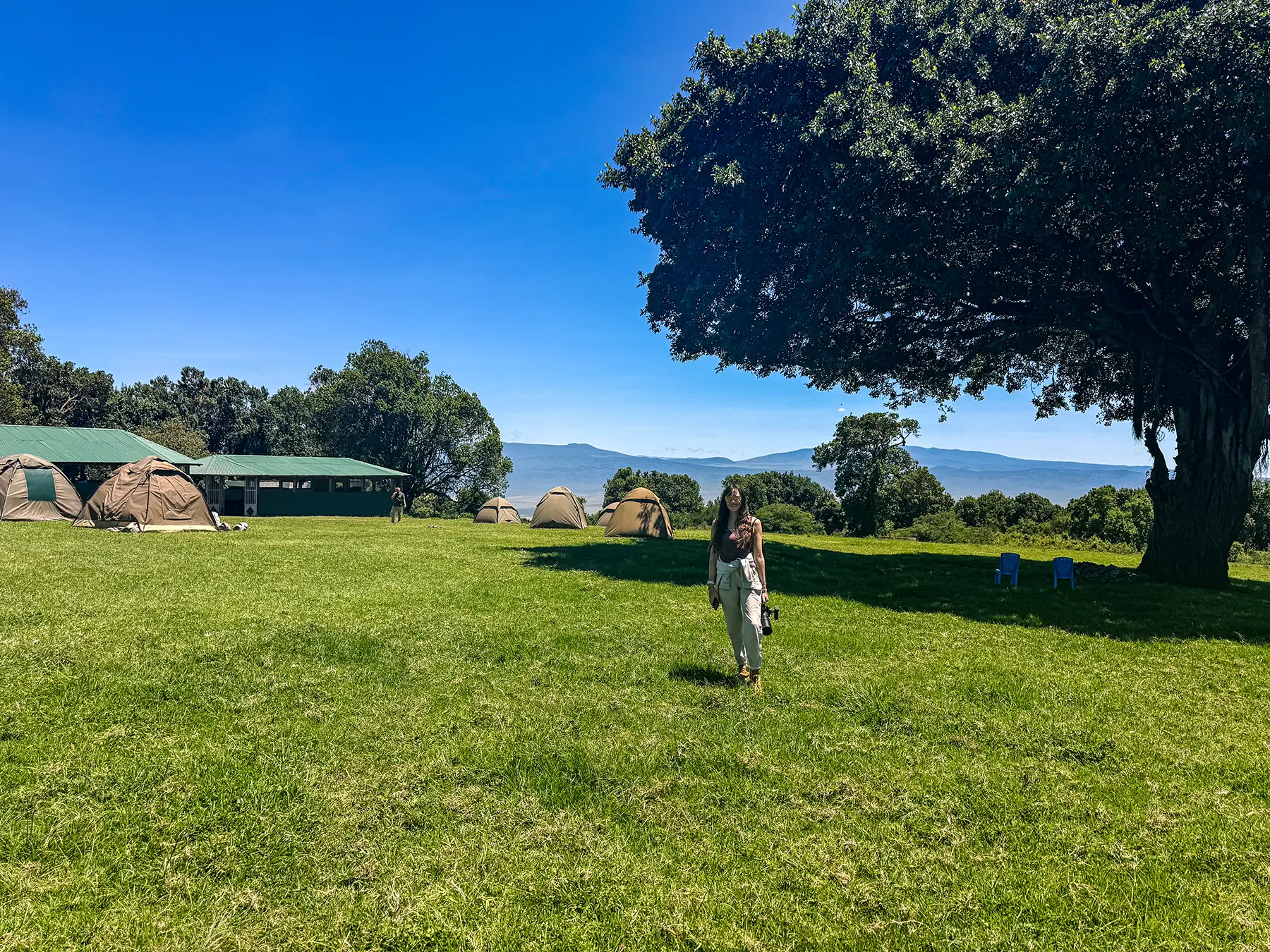 Ella McKendrick walking across a green campsite with Ngorongoro Conservation Area and the crater hills in the background in Tanzania