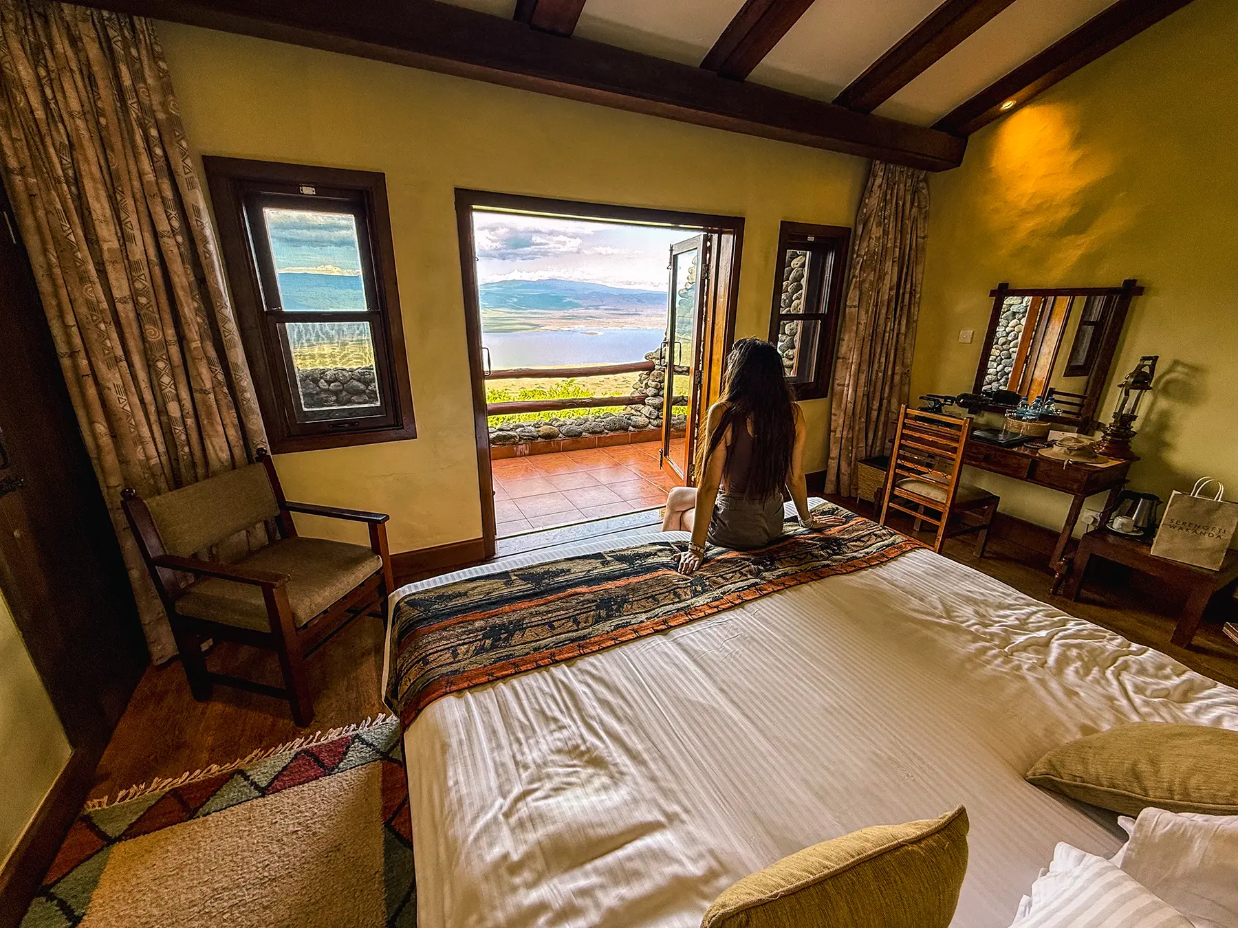 Ella McKendrick sitting on a bed gazing through open terrace doors at the Ngorongoro Crater in the Ngorongoro Conservation Area, Tanzania