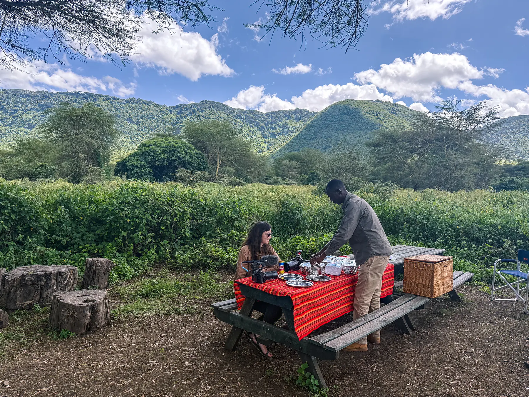 Ella McKendrick being served at a picnic table by a guide against a backdrop of green hills in Ngorongoro Crater, Tanzania