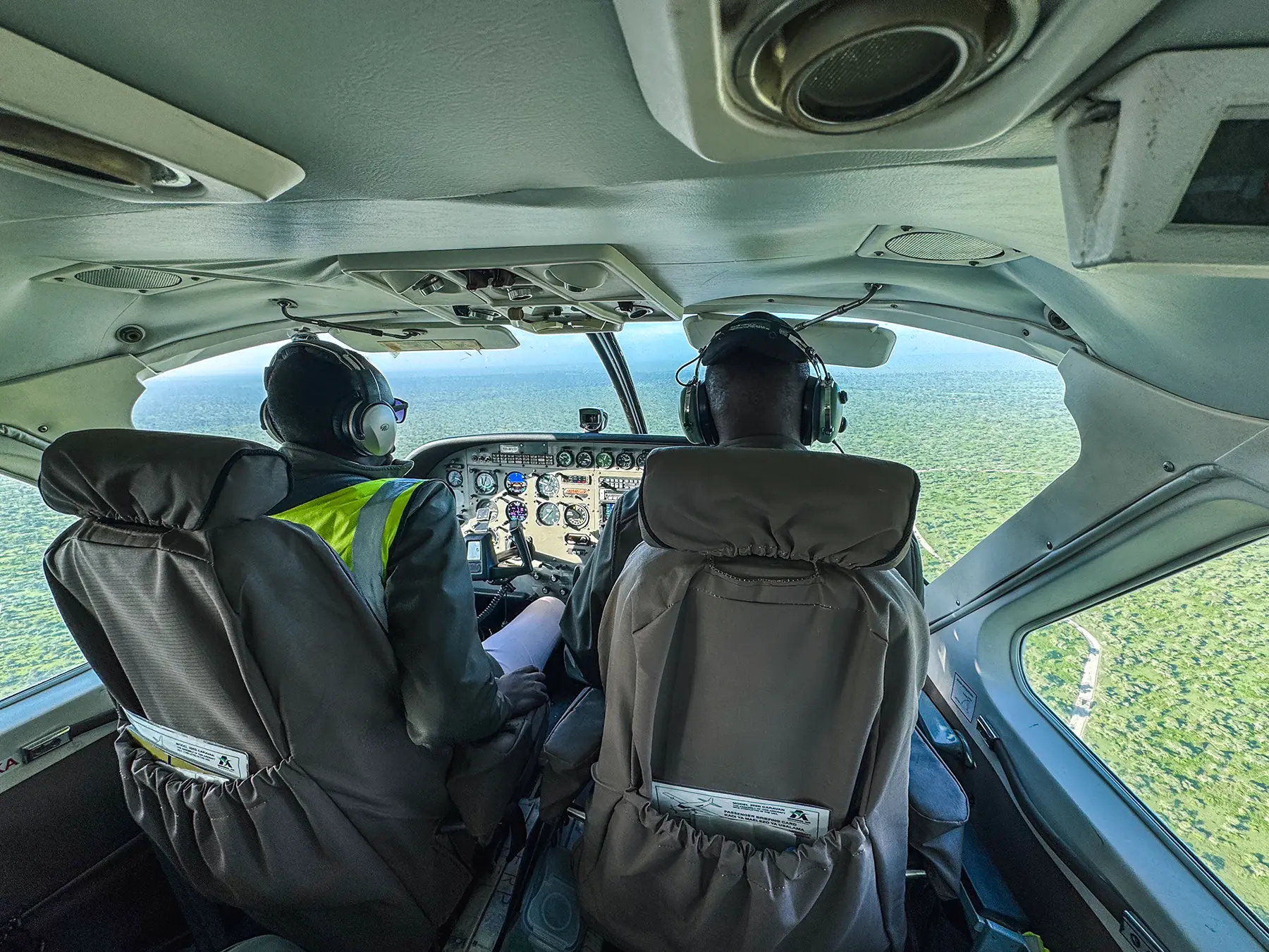 View from behind two pilots in a small bush plane flying over woodland in Tanzania