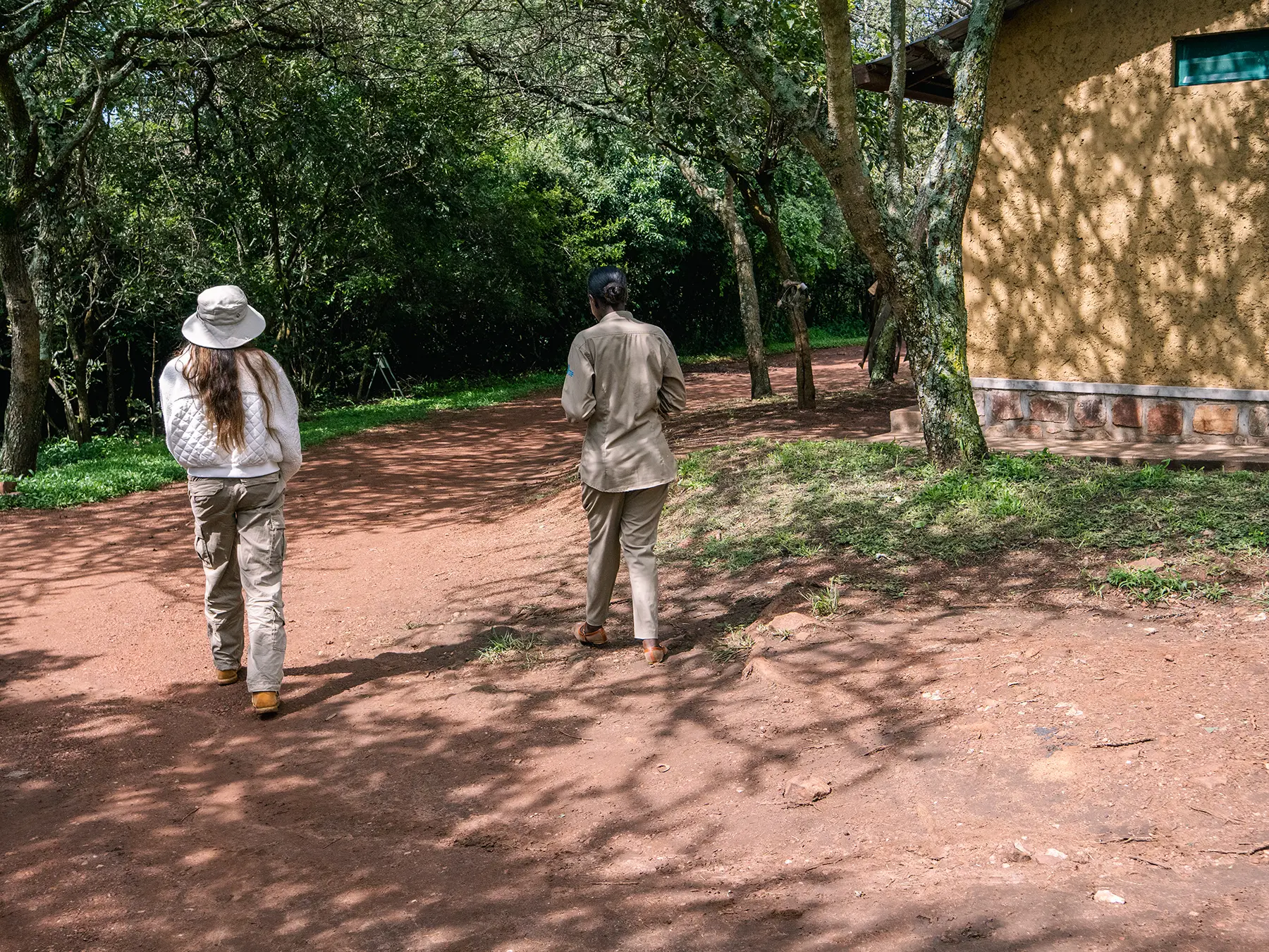 Ella McKendrick walking with the HQ manager past mud-walled buildings at Akagera National Park headquarters, Rwanda