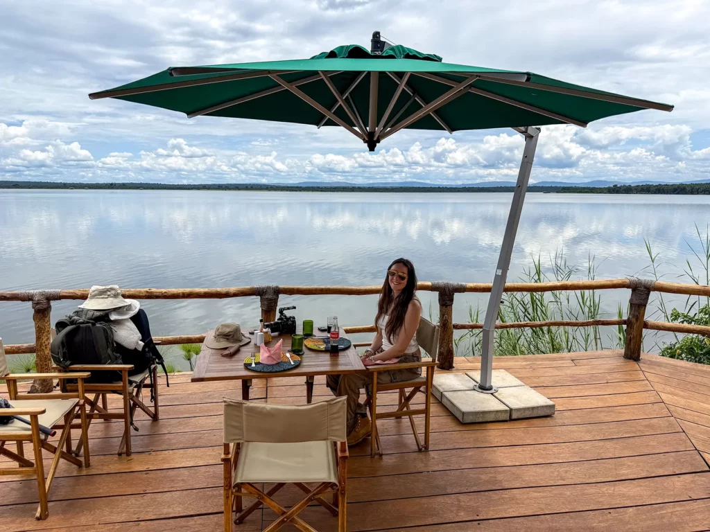 Ella McKendrick at lakeside lunch table under green parasol with Lake Ihema behind at Ruzizi Tented Camp in Akagera National Park, Rwanda