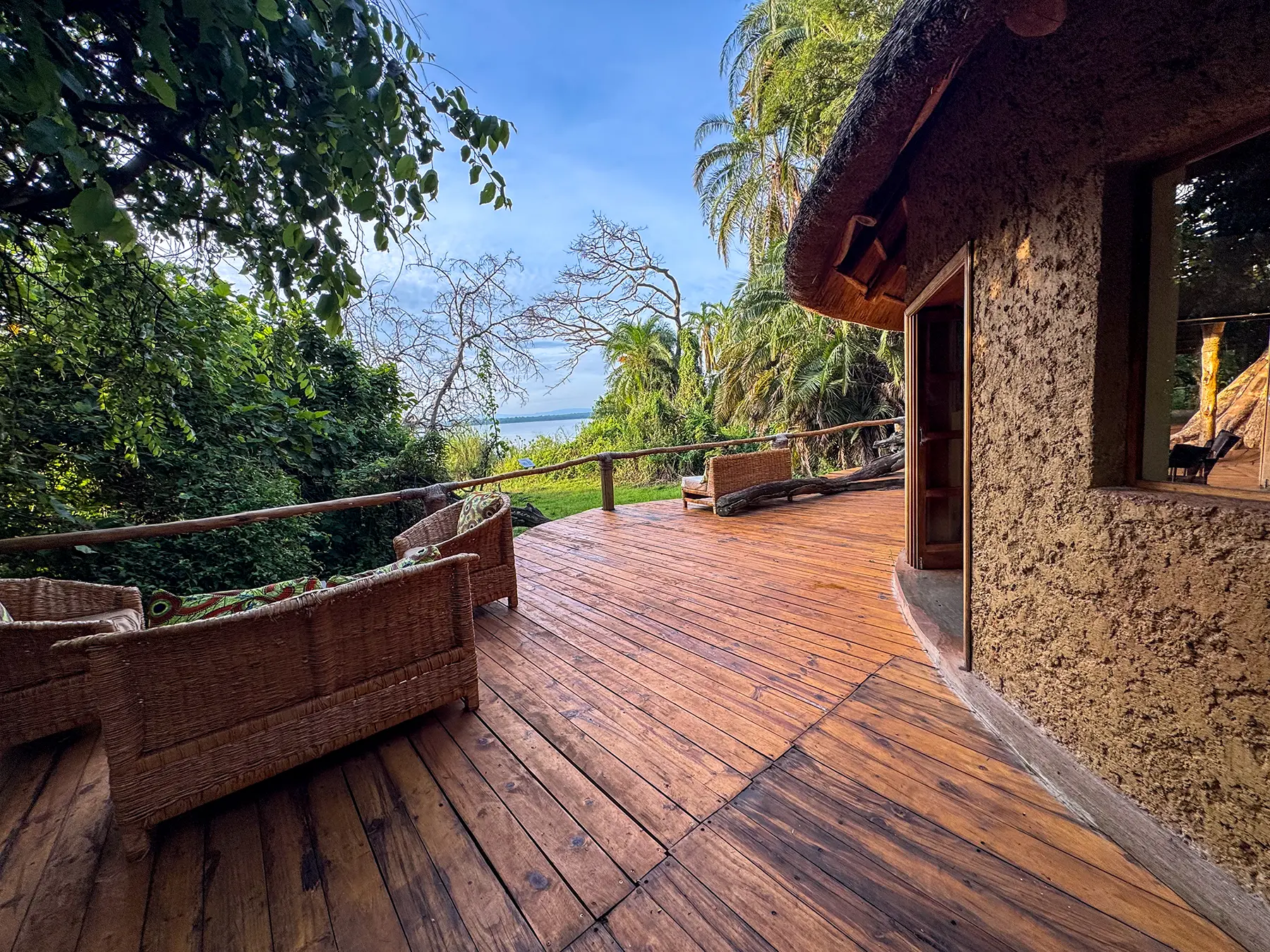 Wooden lounge deck with wicker chairs overlooking Lake Ihema through the trees at Ruzizi Tented Camp in Akagera National Park, Rwanda