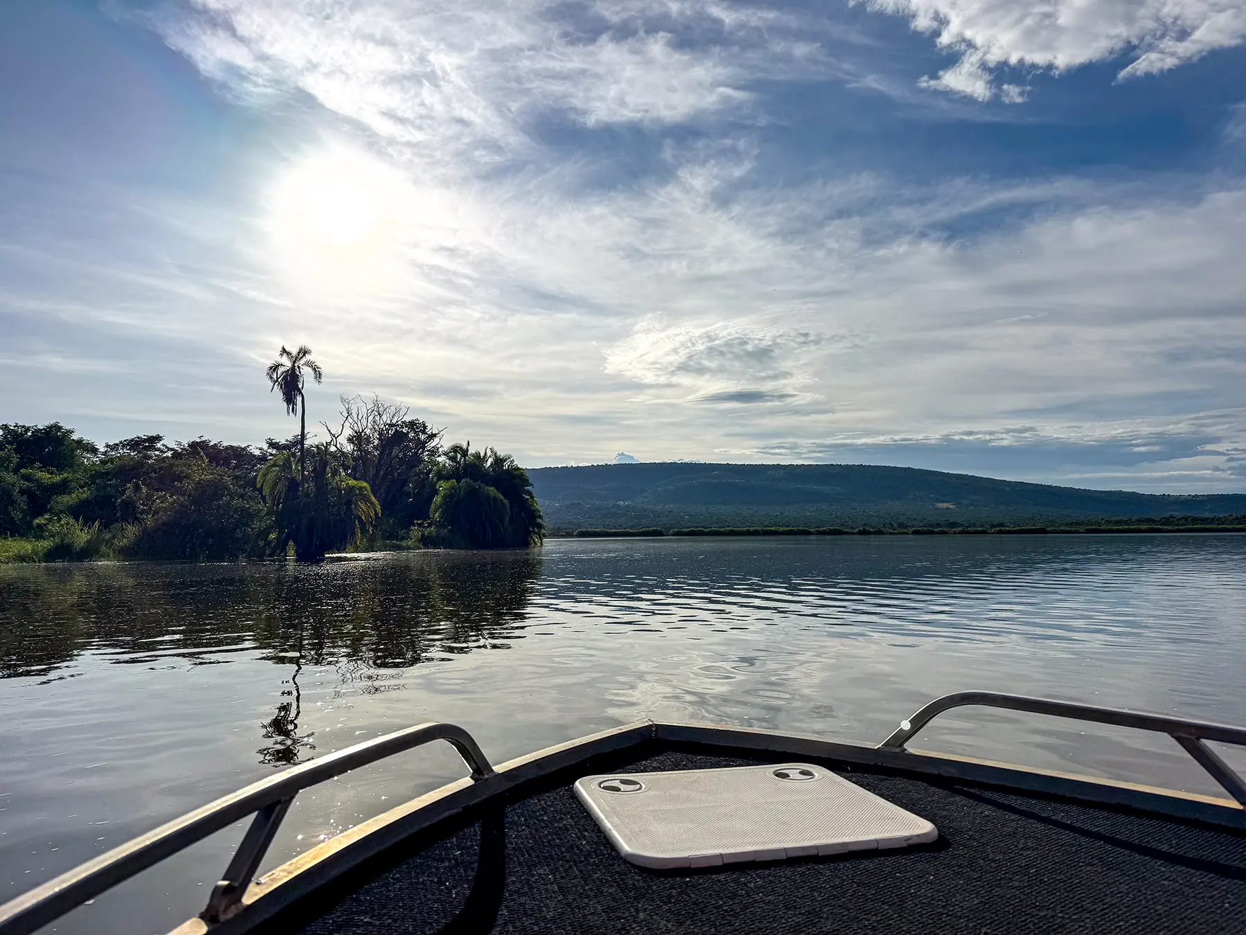 View from boat bow across calm water toward palm island at Lake Ihema in Akagera, Rwanda