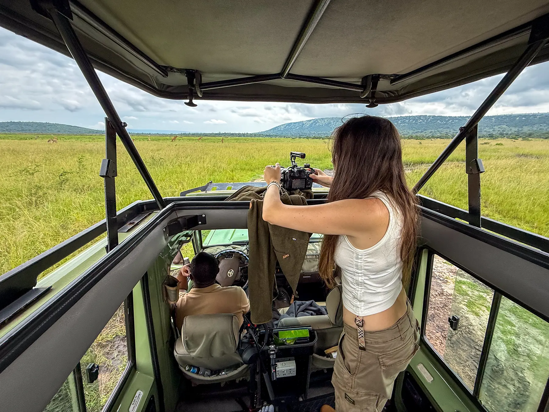 Ella McKendrick filming with camera from open roof safari vehicle on safari in Akagera National Park, Rwanda