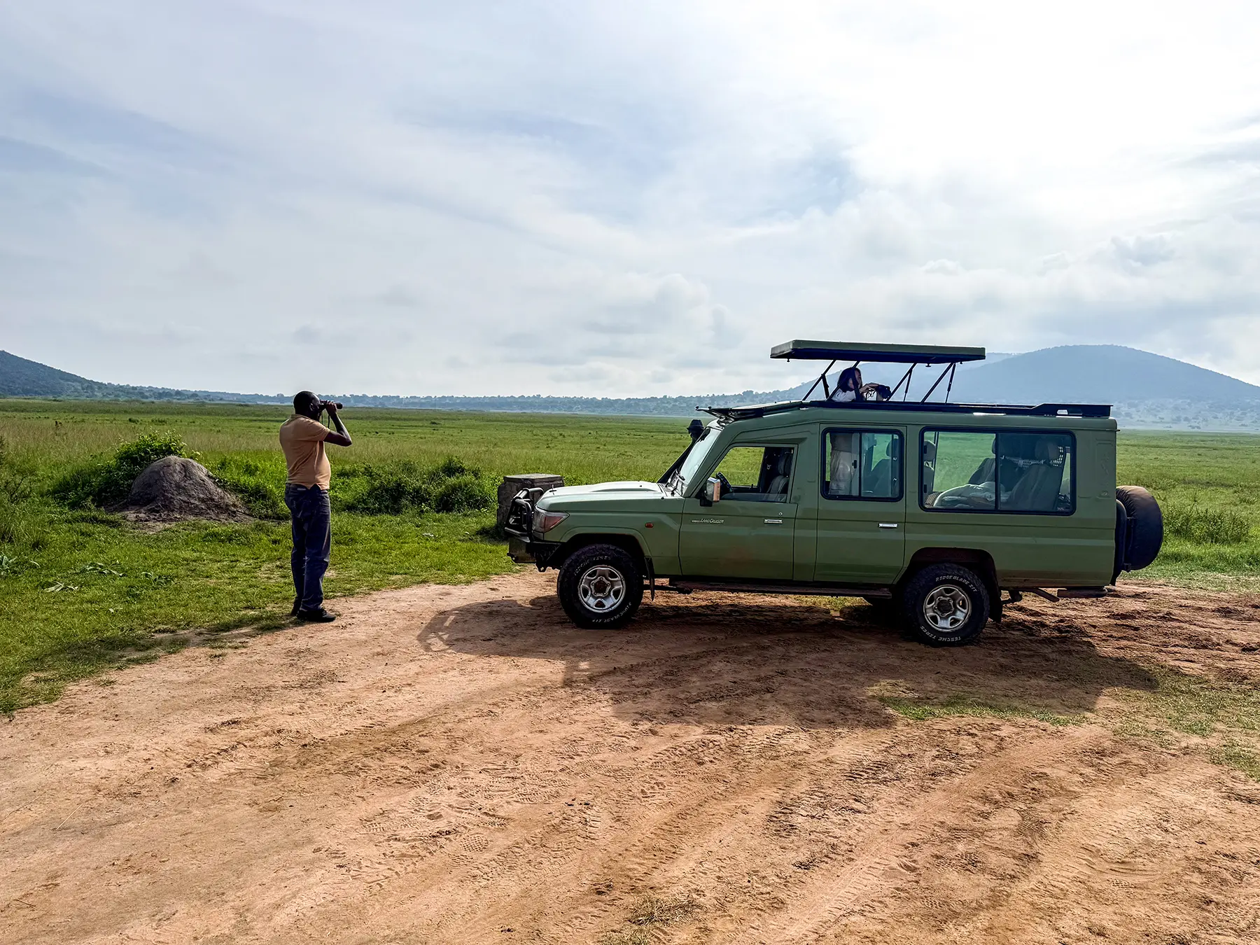 Local Rwandan safari guide with binoculars beside a green Land Cruiser on safari in Akagera National Park, Rwanda