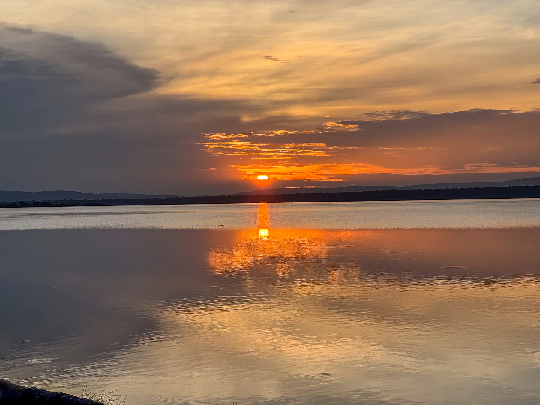 Deep orange sun setting behind hills mirrored on still water at Lake Ihema in Akagera, Rwanda