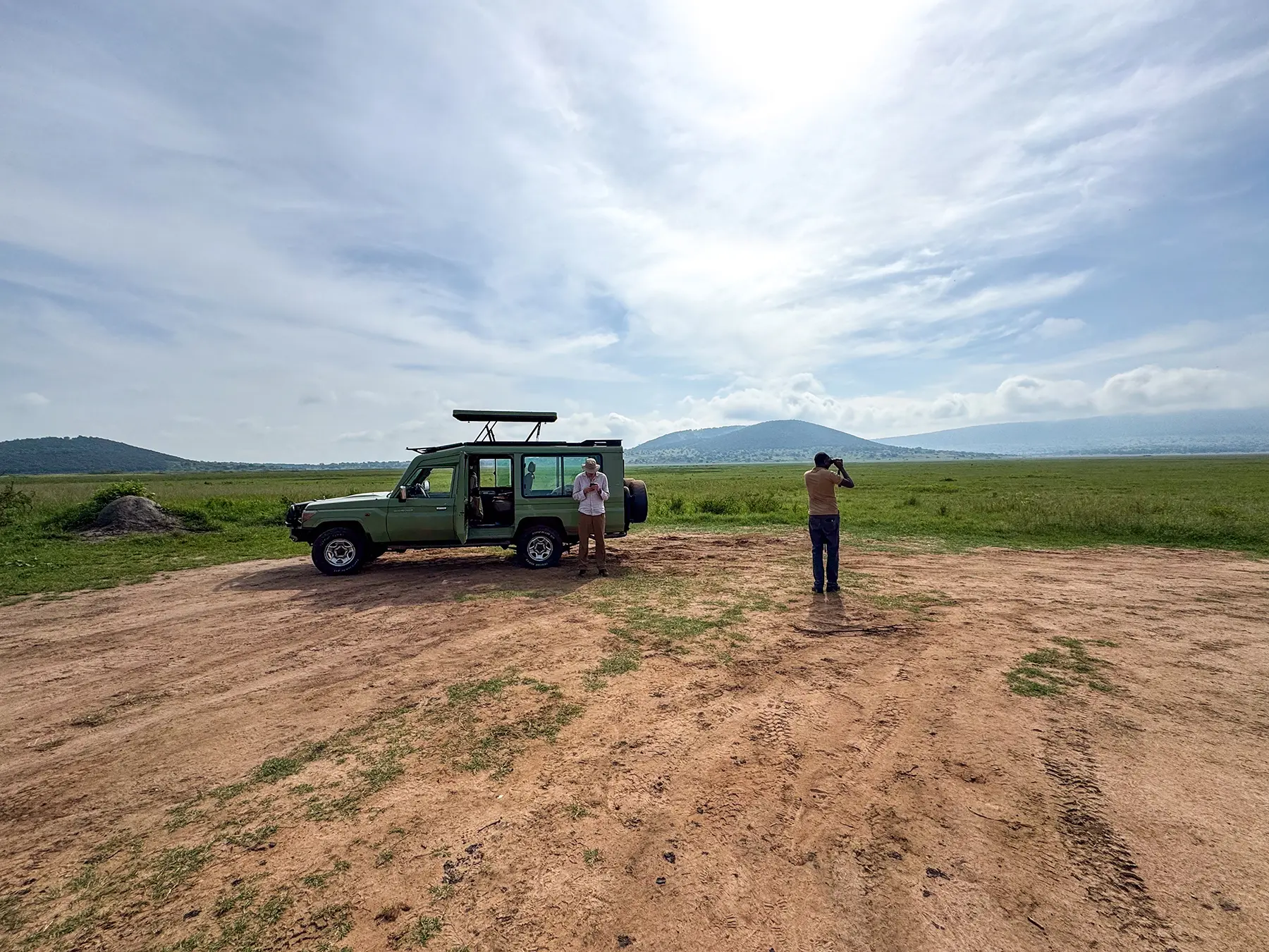 Safari Land Cruiser parked on a clearing with two people photographing on safari in Akagera National Park, Rwanda