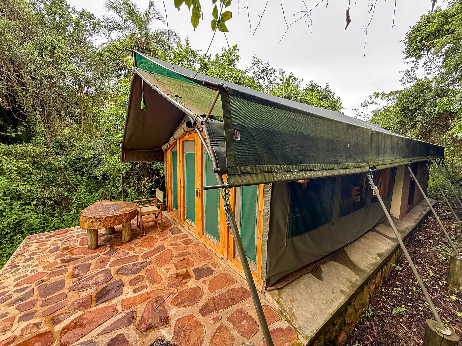 Safari tent exterior with stone patio and forested surroundings at Ruzizi Tented Camp in Akagera National Park, Rwanda