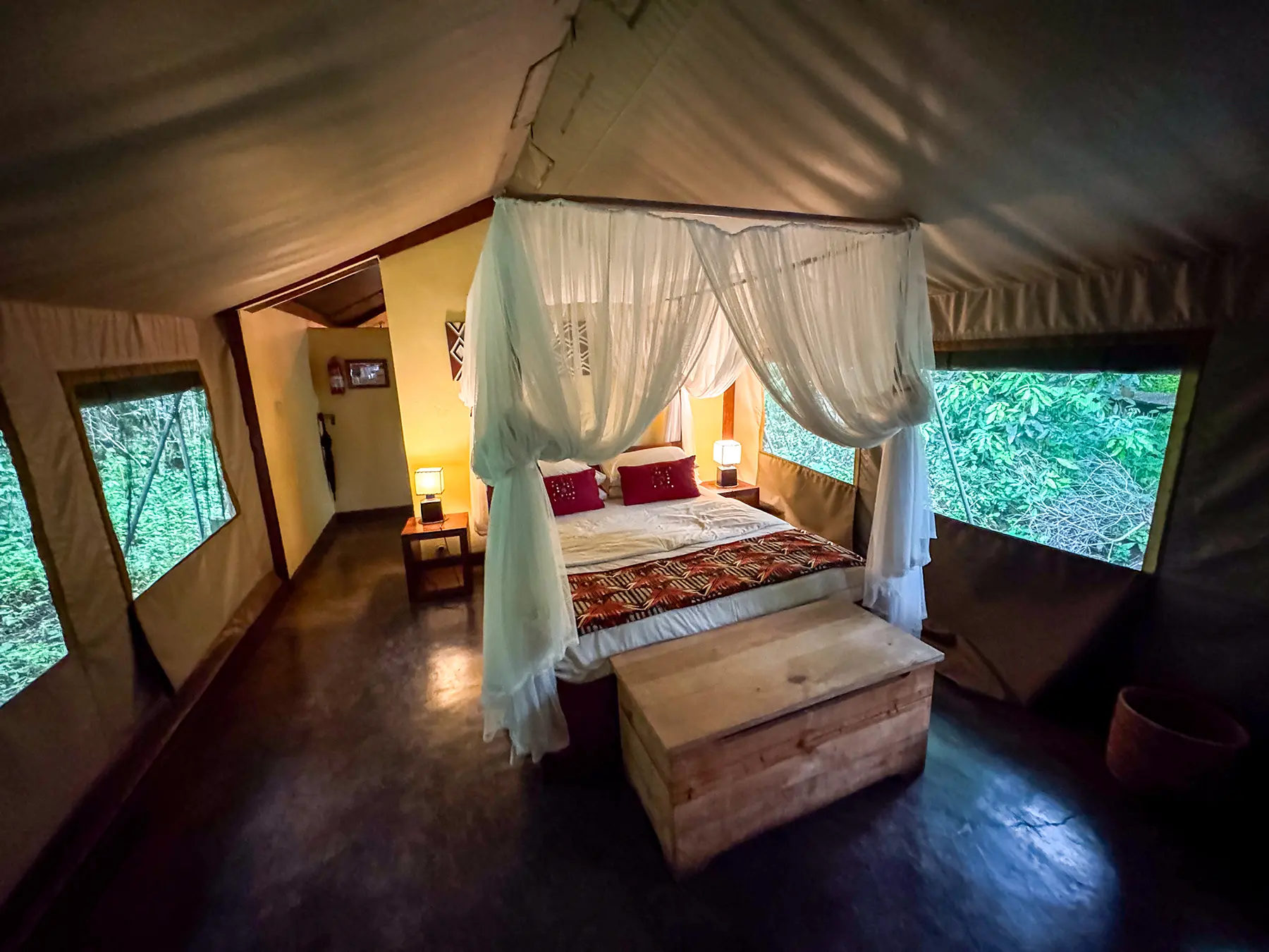 Safari tent interior with canopy bed, mosquito netting and bedside lamps at Ruzizi Tented Camp in Akagera National Park, Rwanda
