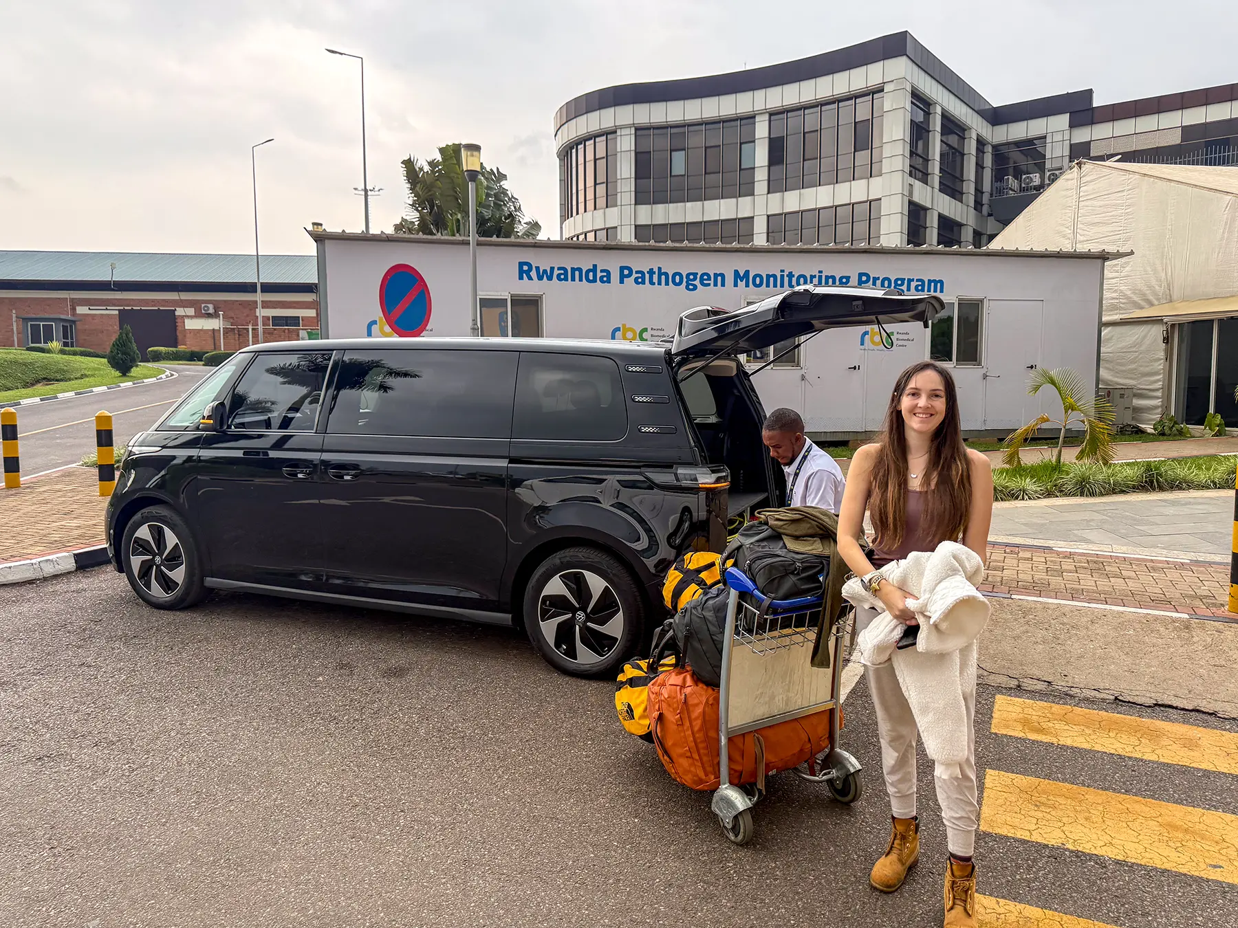 Ella McKendrick beside black transfer van with luggage trolley at Kigali International Airport, Rwanda