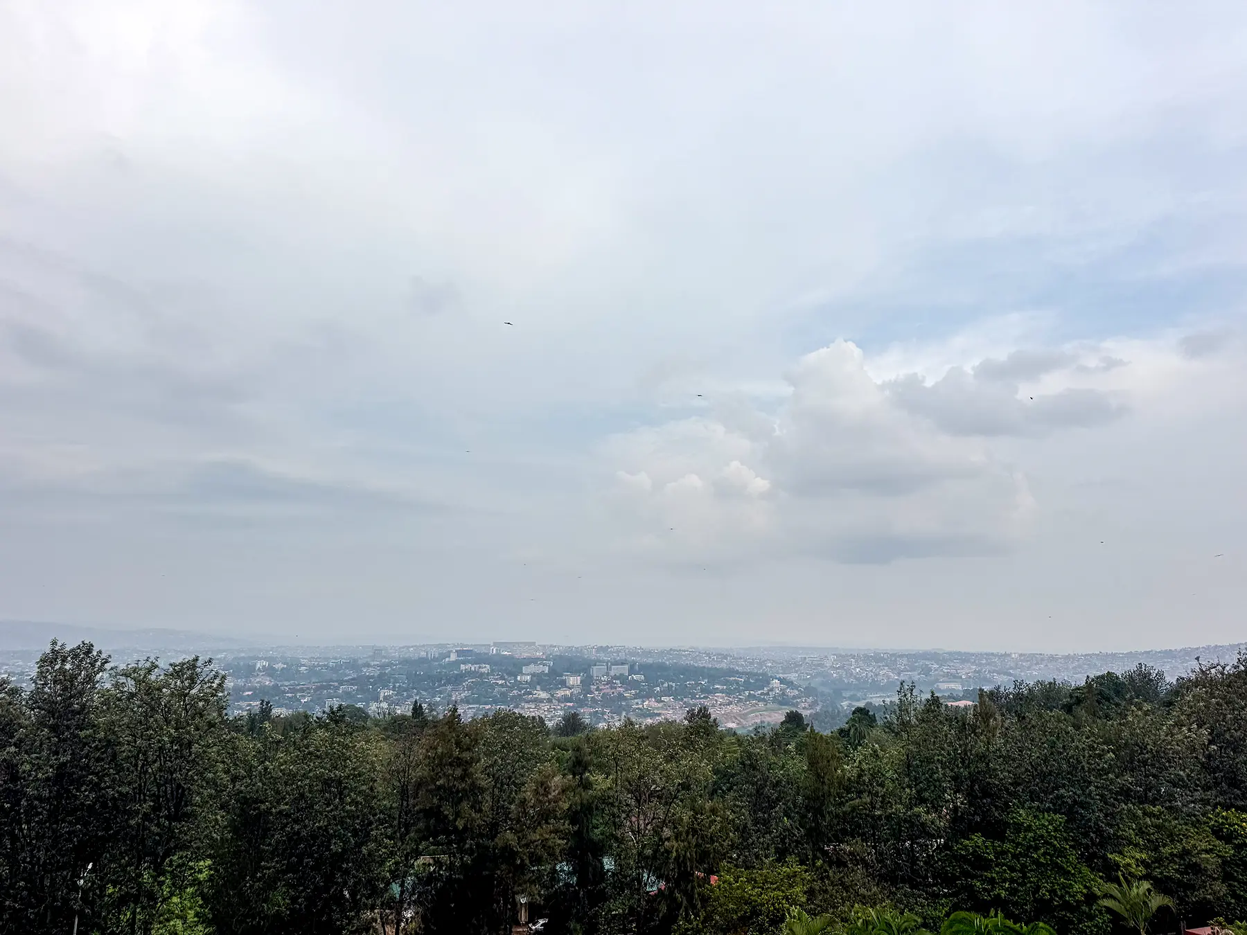 Hazy panorama of city sprawl across hills under cloudy sky at hilltop viewpoint in Kigali, Rwanda