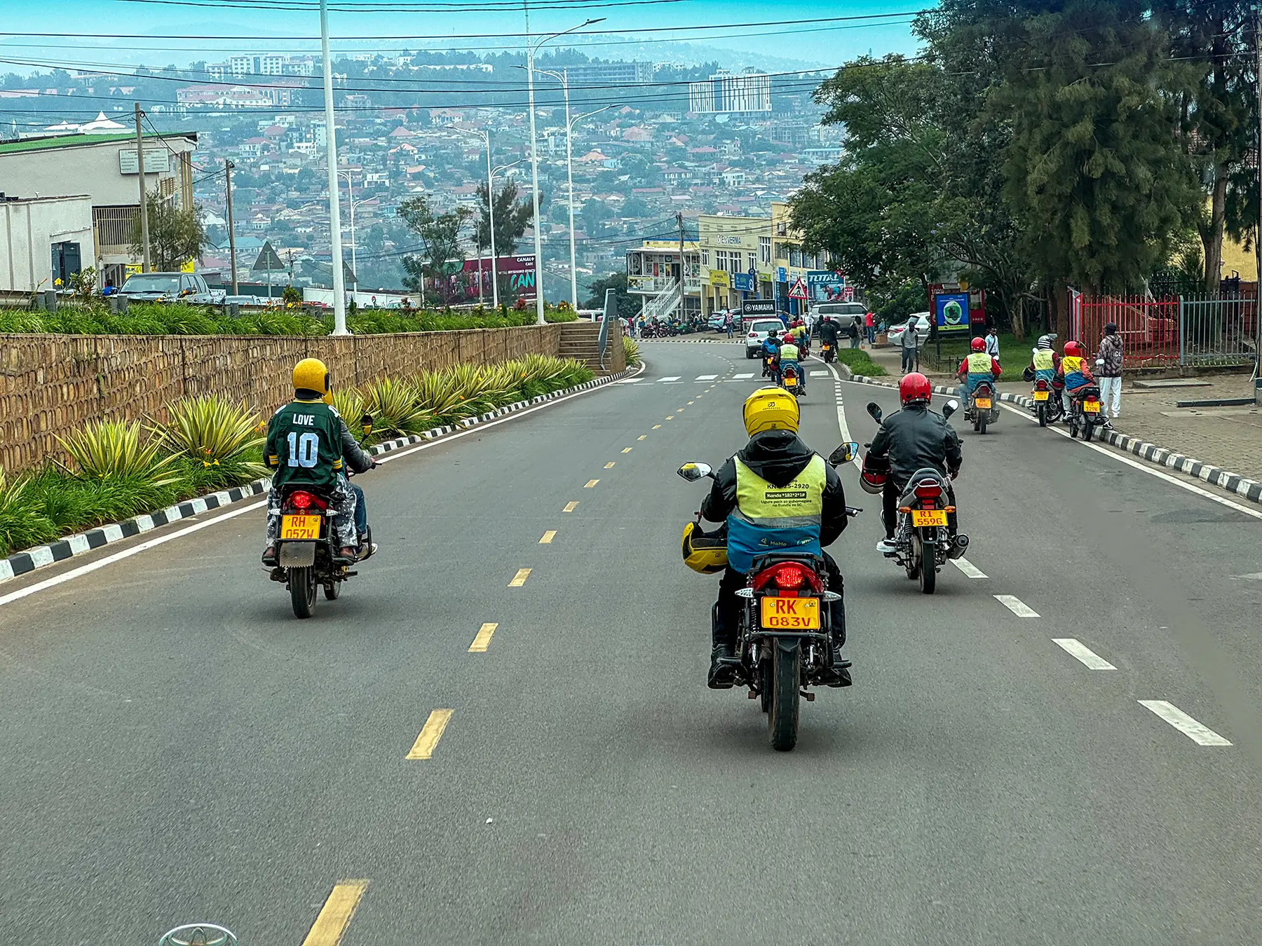 Group of motorbike taxis riding down a wide road towards distant hills at boulevard in Kigali, Rwanda