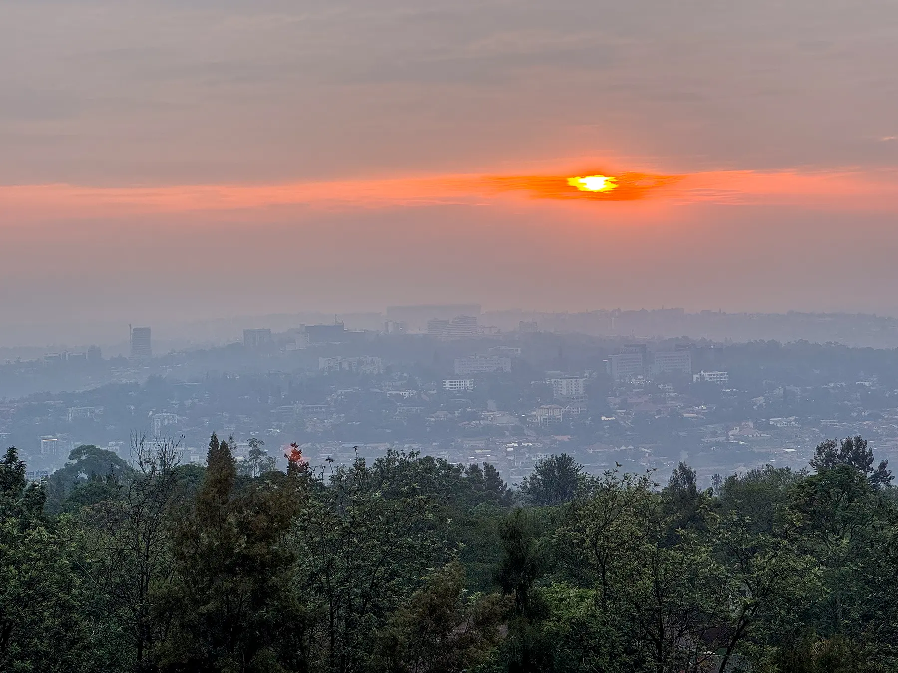Setting sun breaking through clouds over hazy hilltop city at viewpoint in Kigali, Rwanda