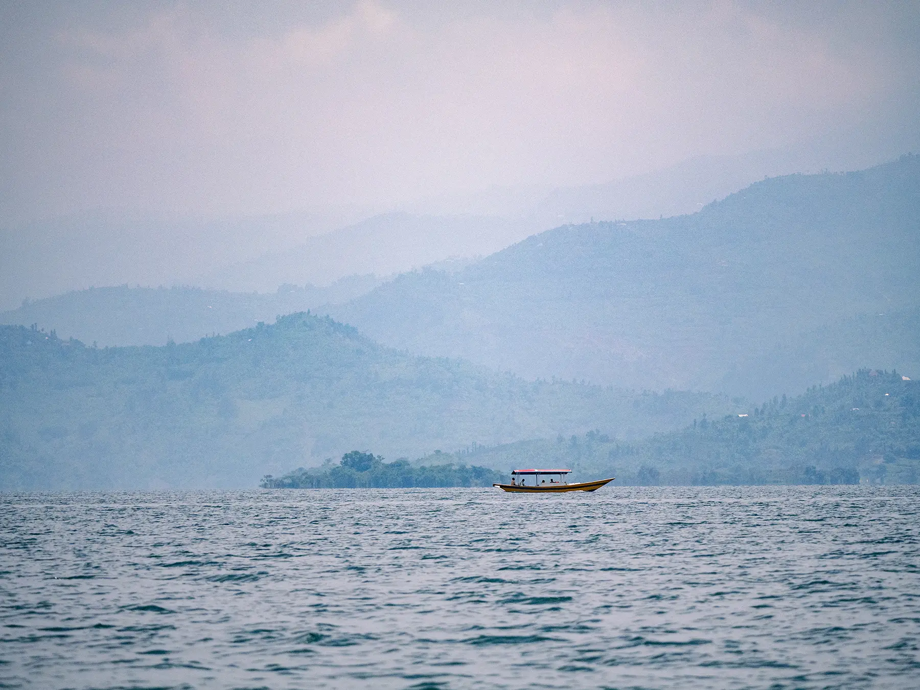 Lone boat on misty water beneath layered hills at Lake Kivu, Rwanda
