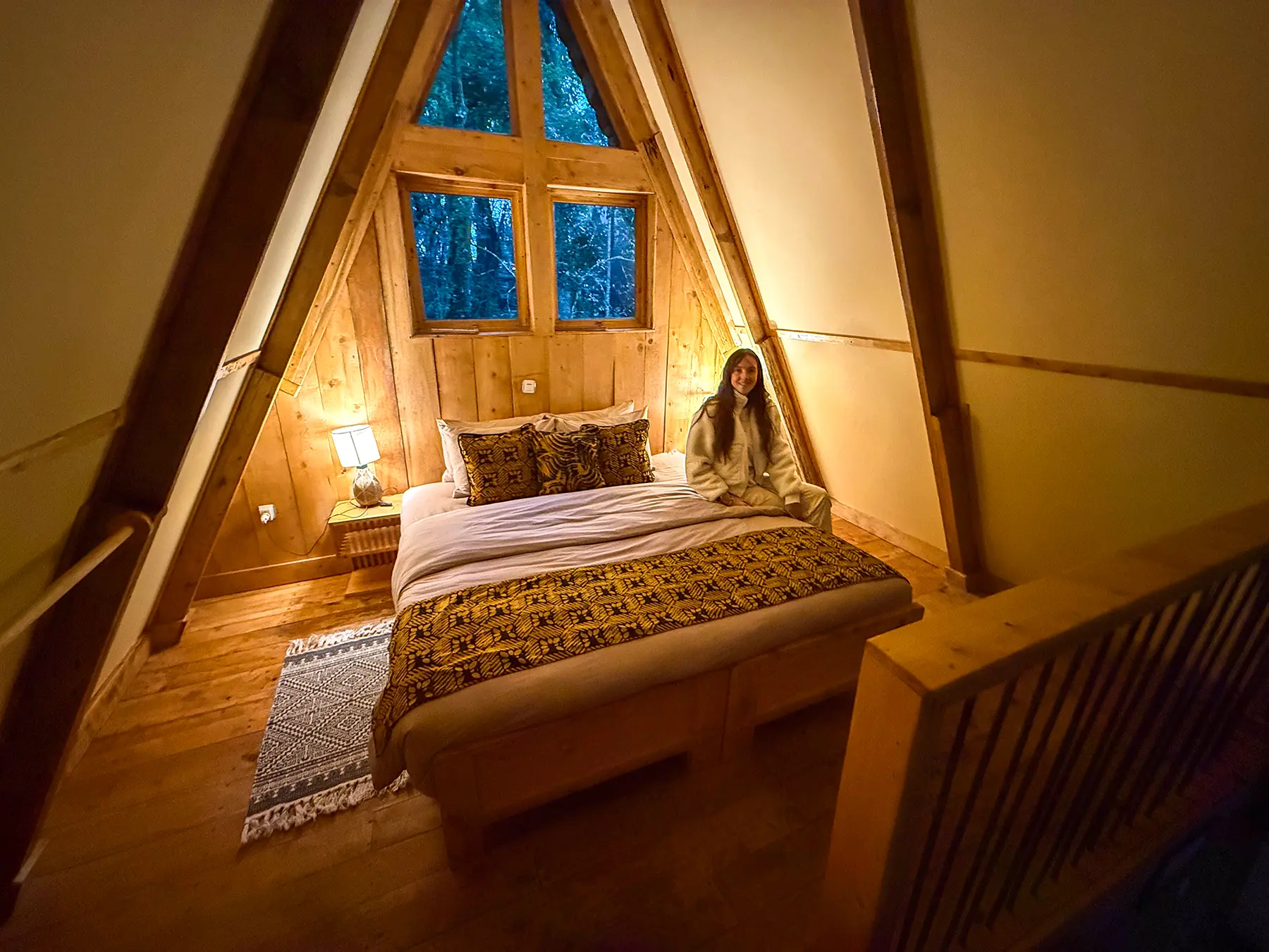Ella McKendrick sitting on bed in A-frame wooden cabin bedroom at Munazi Lodge in Nyungwe National Park, Rwanda