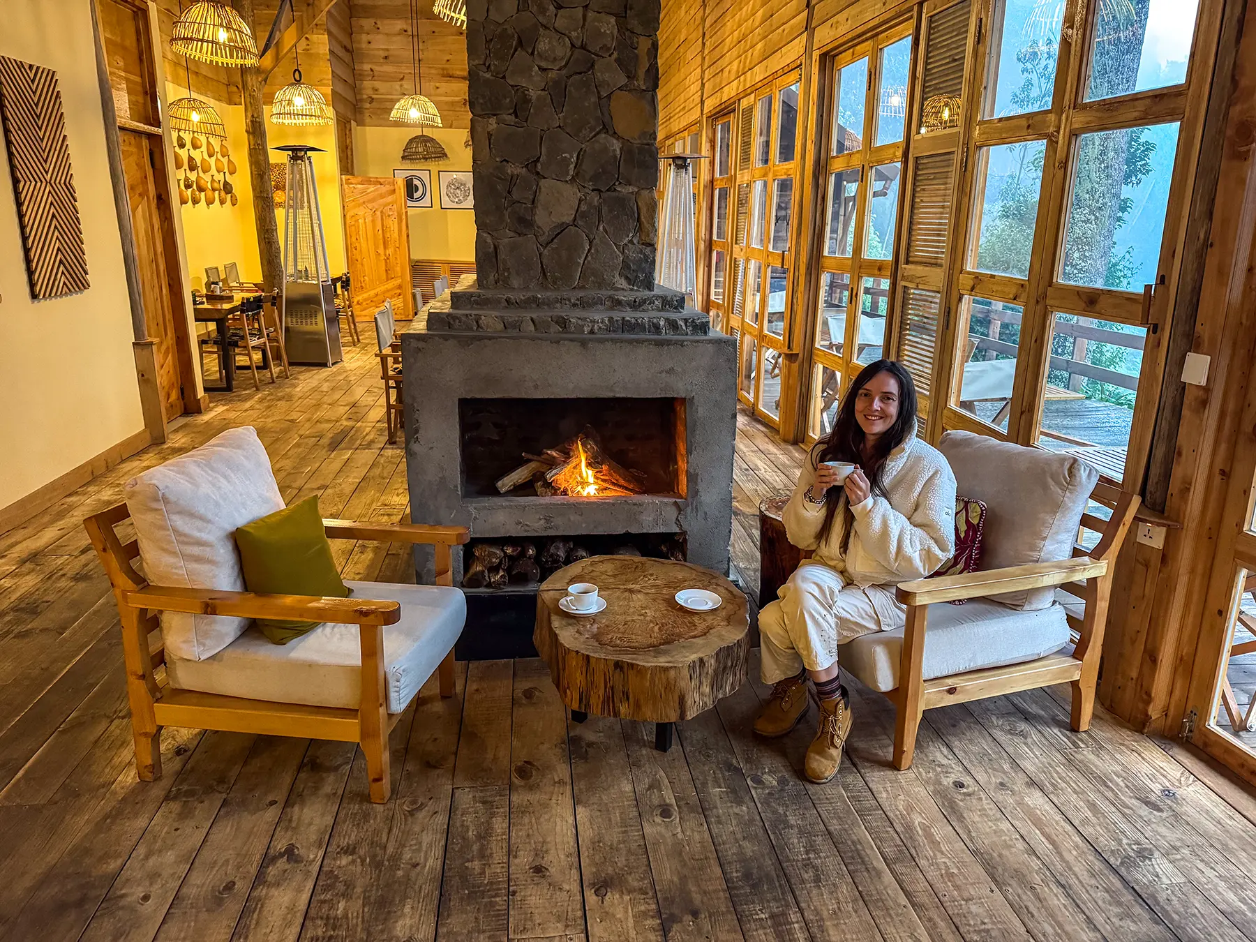 Ella McKendrick holding coffee cup beside lit fireplace in lodge lounge at Munazi Lodge in Nyungwe National Park, Rwanda