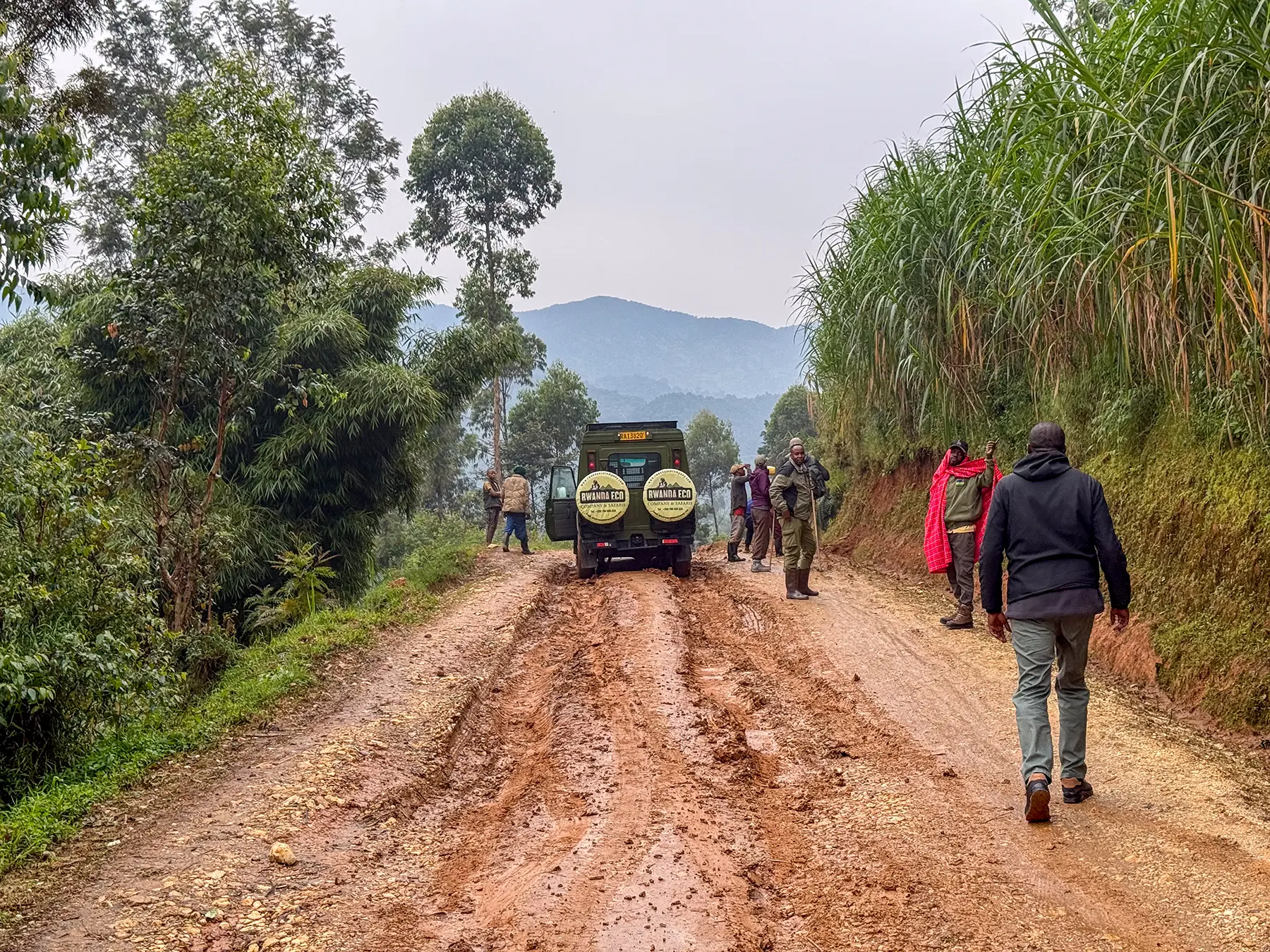 Group walking ahead of our safari vehicle along a muddy approach track at Banda village in Nyungwe National Park, Rwanda