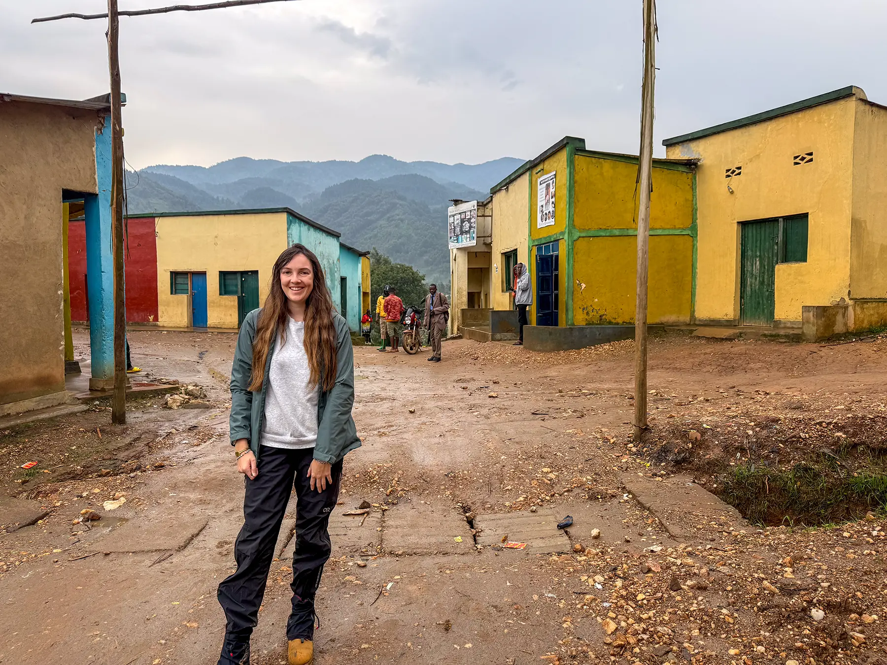 Ella McKendrick standing in a colourful village square with painted buildings at Banda village in Nyungwe National Park, Rwanda